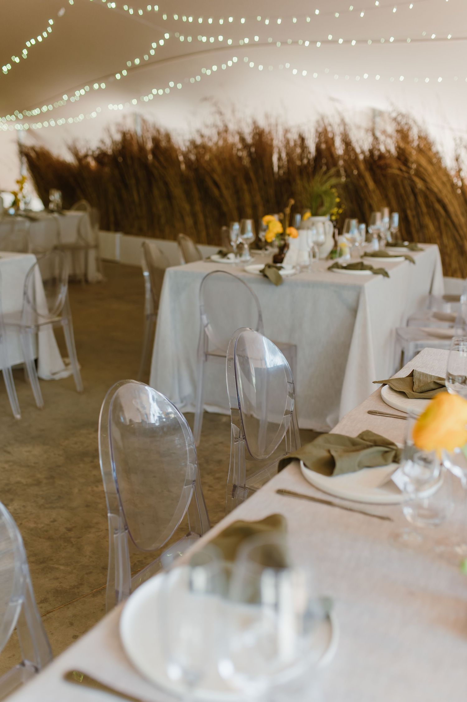 Elegant wedding reception tables with white linens and string lights under a tent.