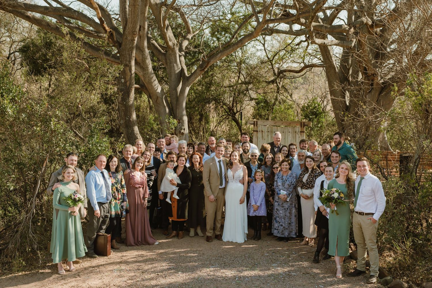 Rustic wooden benches arranged in rows beneath large trees for an outdoor wedding ceremony.