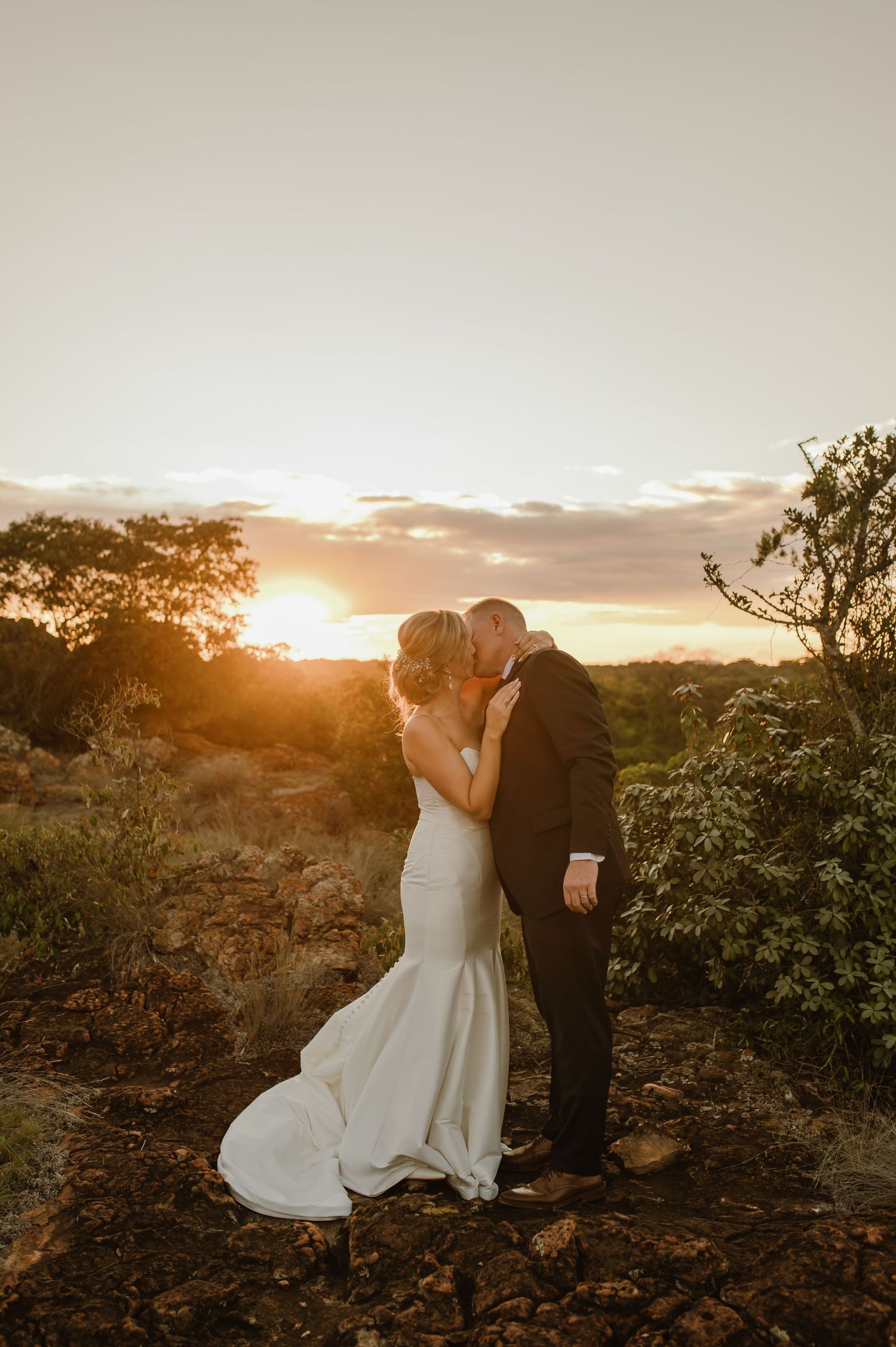 Wedding couple shares romantic moments on rocky terrain during a beautiful sunset photoshoot.
