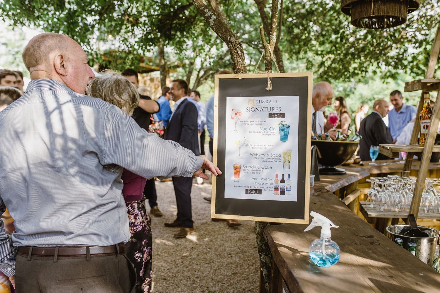 Wedding guests gather around a framed display at an outdoor reception venue.