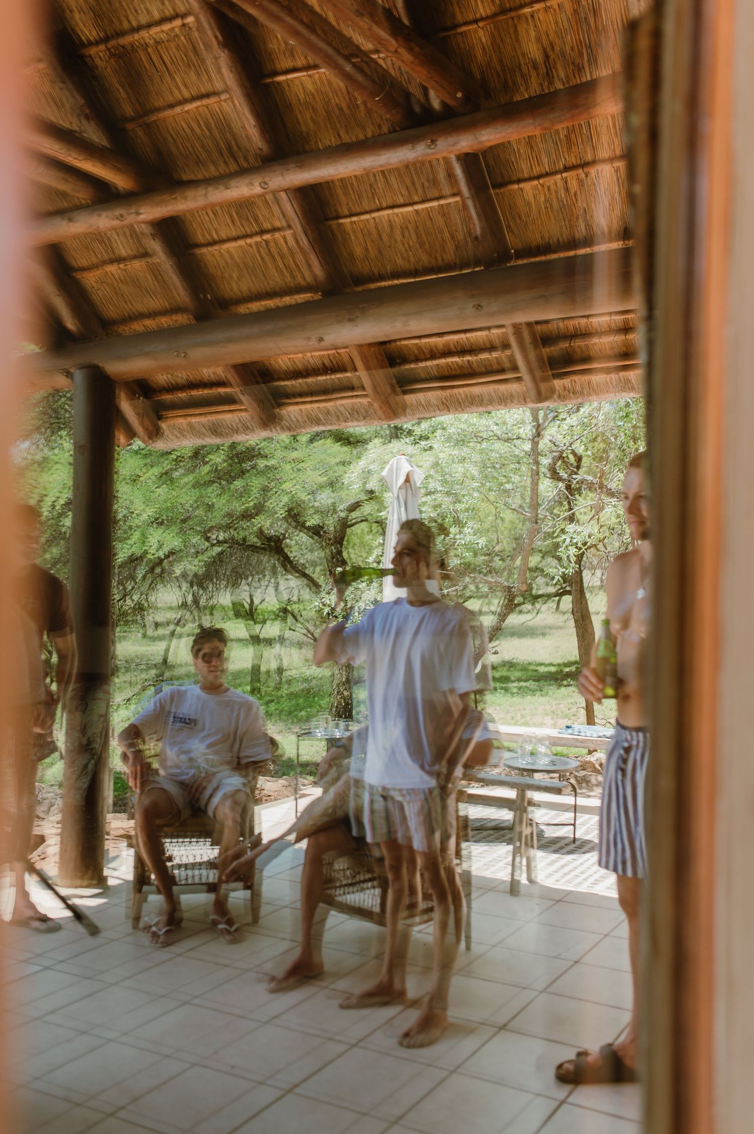 Casual gathering at an outdoor pool table under thatched roof.