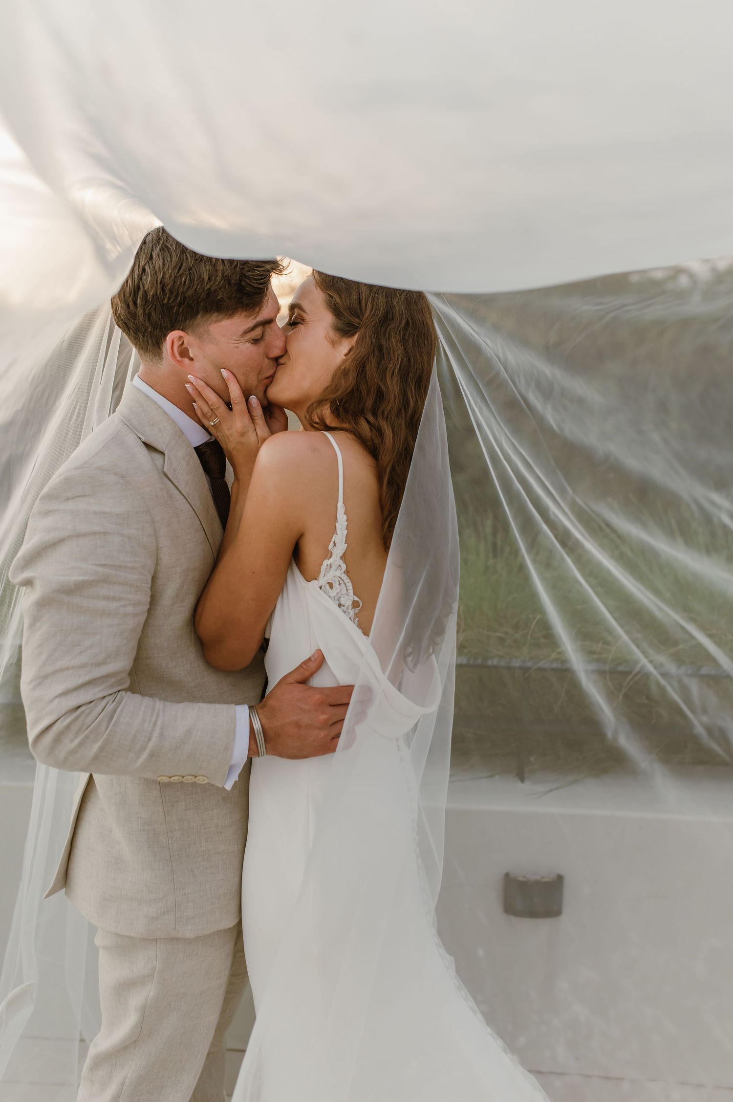 Romantic wedding kiss captured through ethereal veil during outdoor photo session.