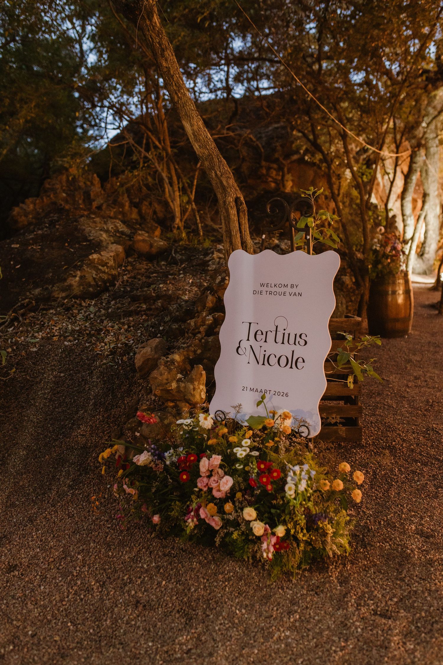 Wedding welcome sign for Tertius and Nicole dated 21 Maart 2024 surrounded by colorful flowers outdoors.