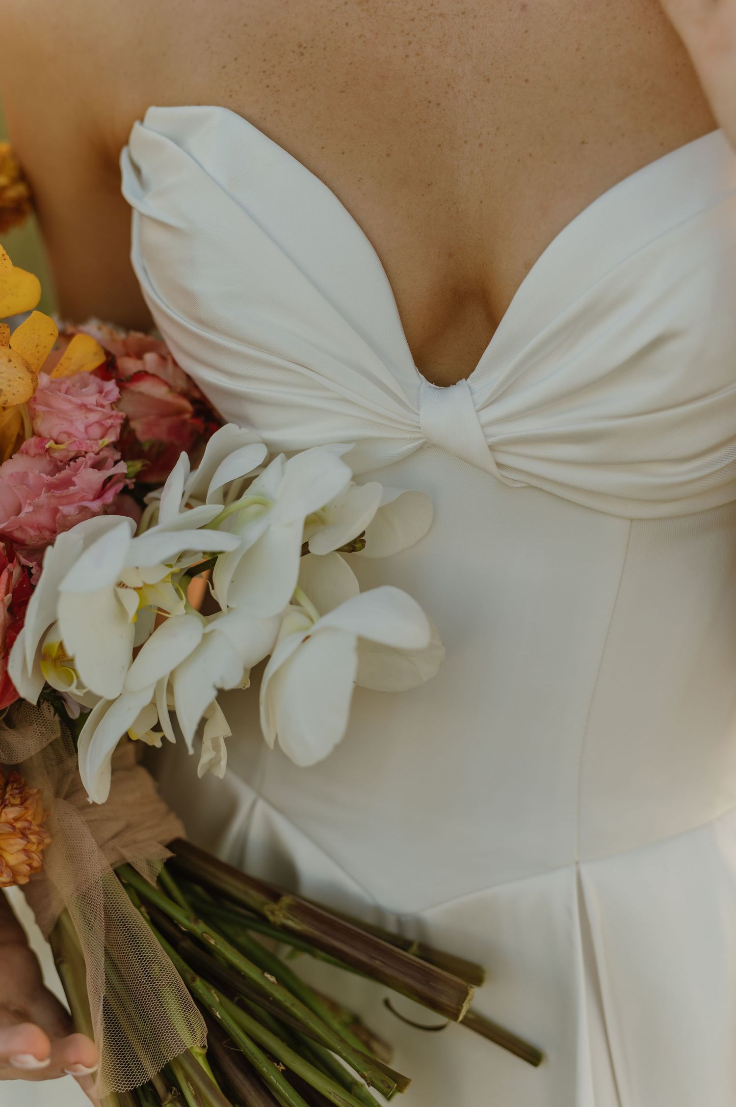 Close-up of bride in sweetheart neckline white gown holding white orchid and colorful wedding bouquet.