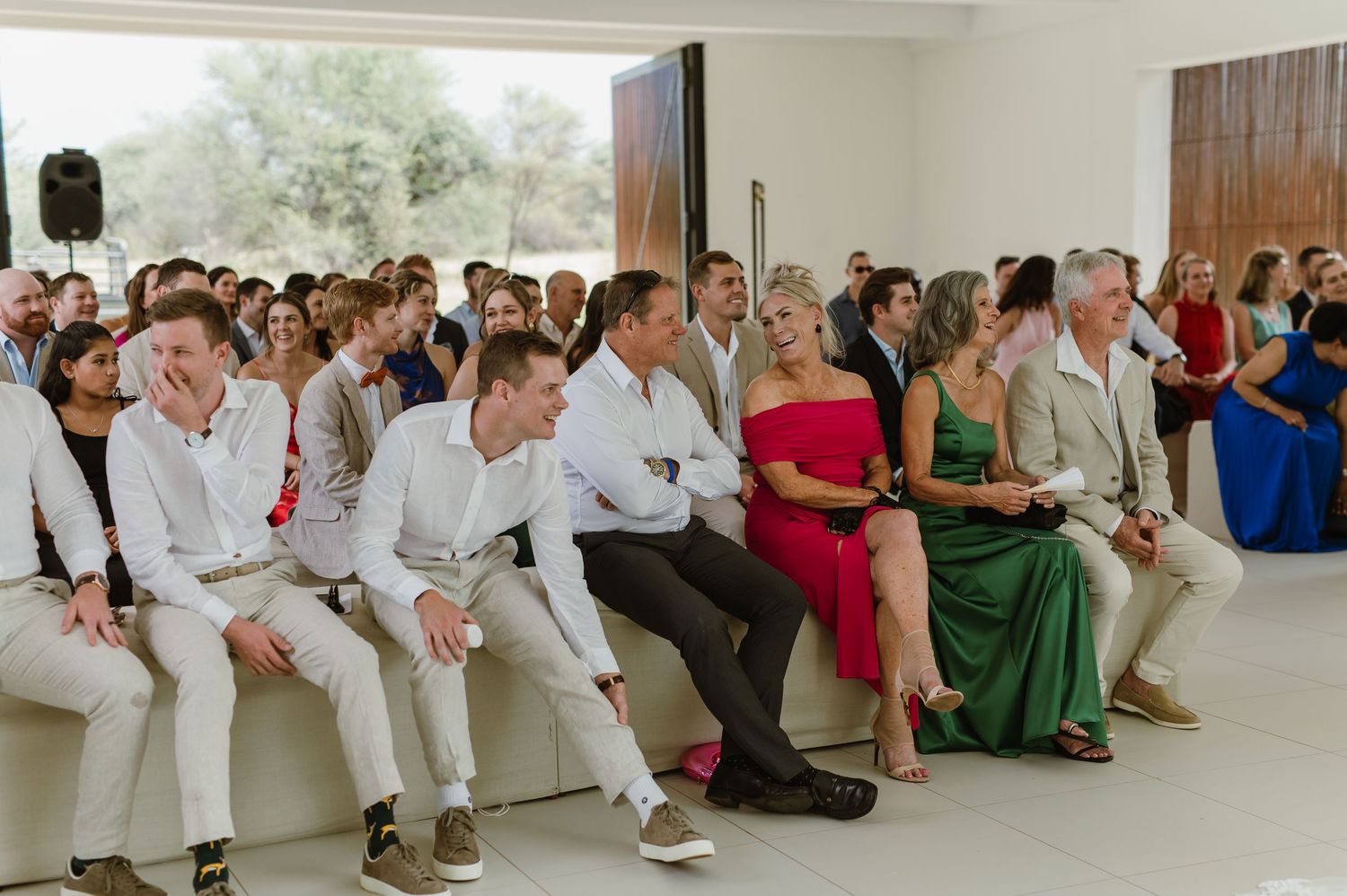 Wedding guests seated in rows inside a bright modern venue with white walls and ceiling.