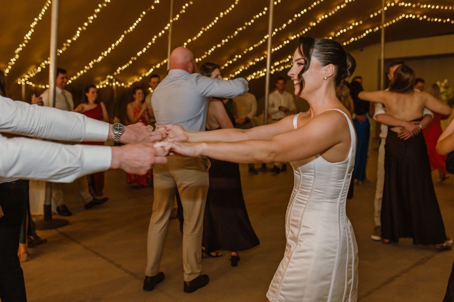 Wedding guests dancing and celebrating on the dance floor under glowing string lights.