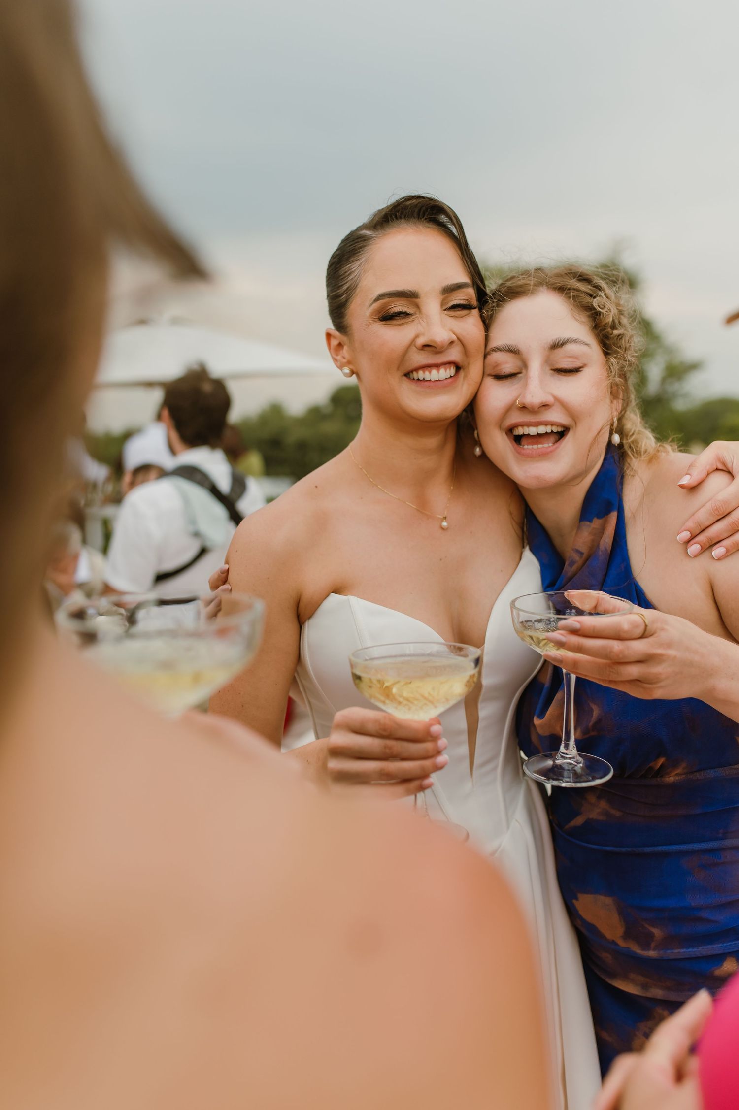 Two people in formal attire share drinks and laughter during an outdoor celebration event.