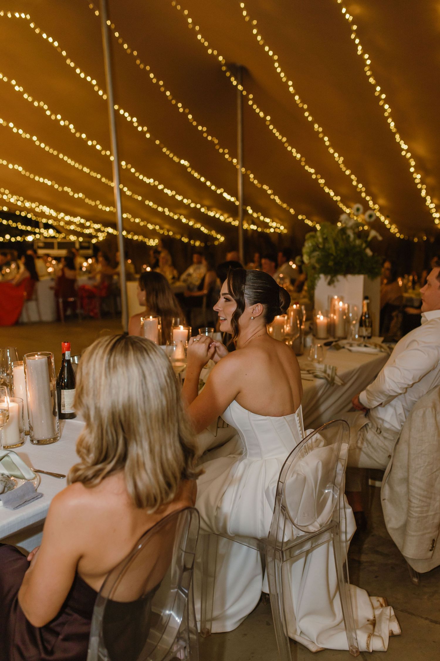 Wedding guests raising glasses in a toast under twinkling lights at an outdoor reception.