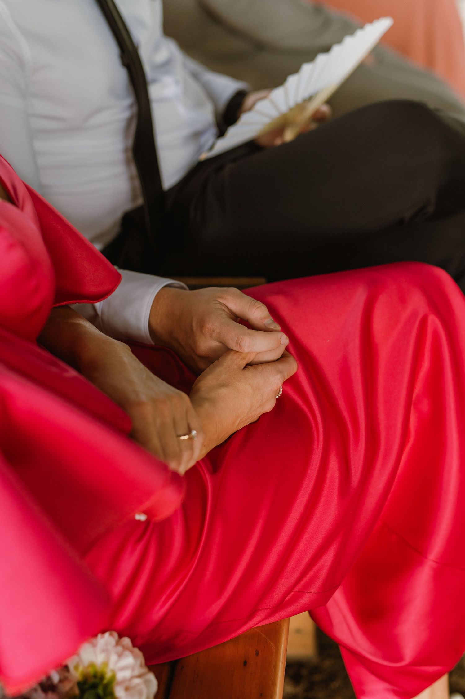 Close-up of a couple holding hands, the woman wearing a vibrant red satin dress at a wedding ceremony.