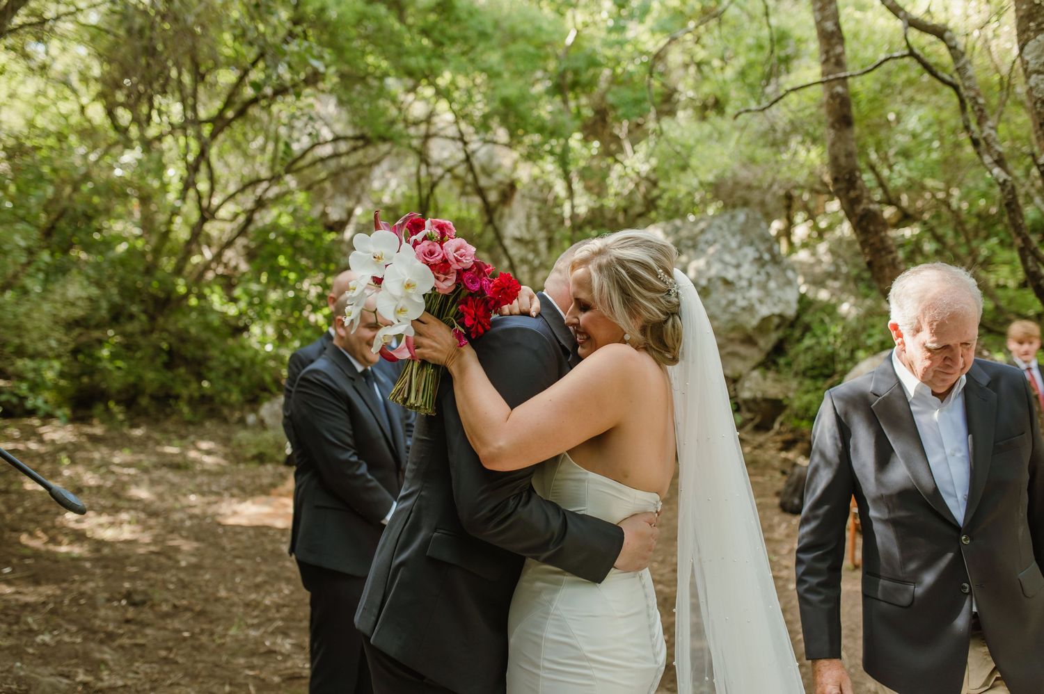 Intimate wedding ceremony moment in a forest setting with red and white bouquet.