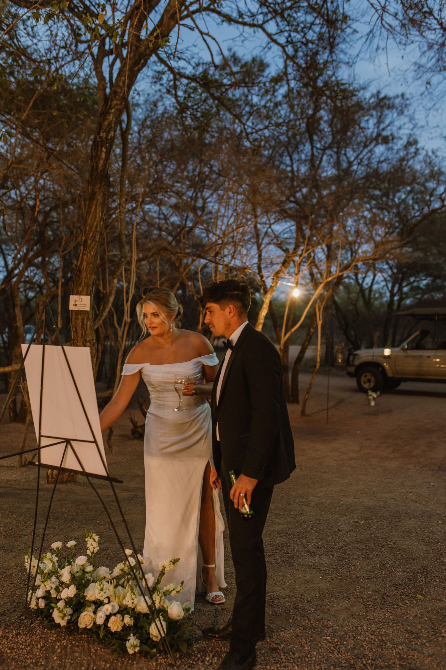 Couple viewing wedding seating chart decorated with white flowers at twilight.