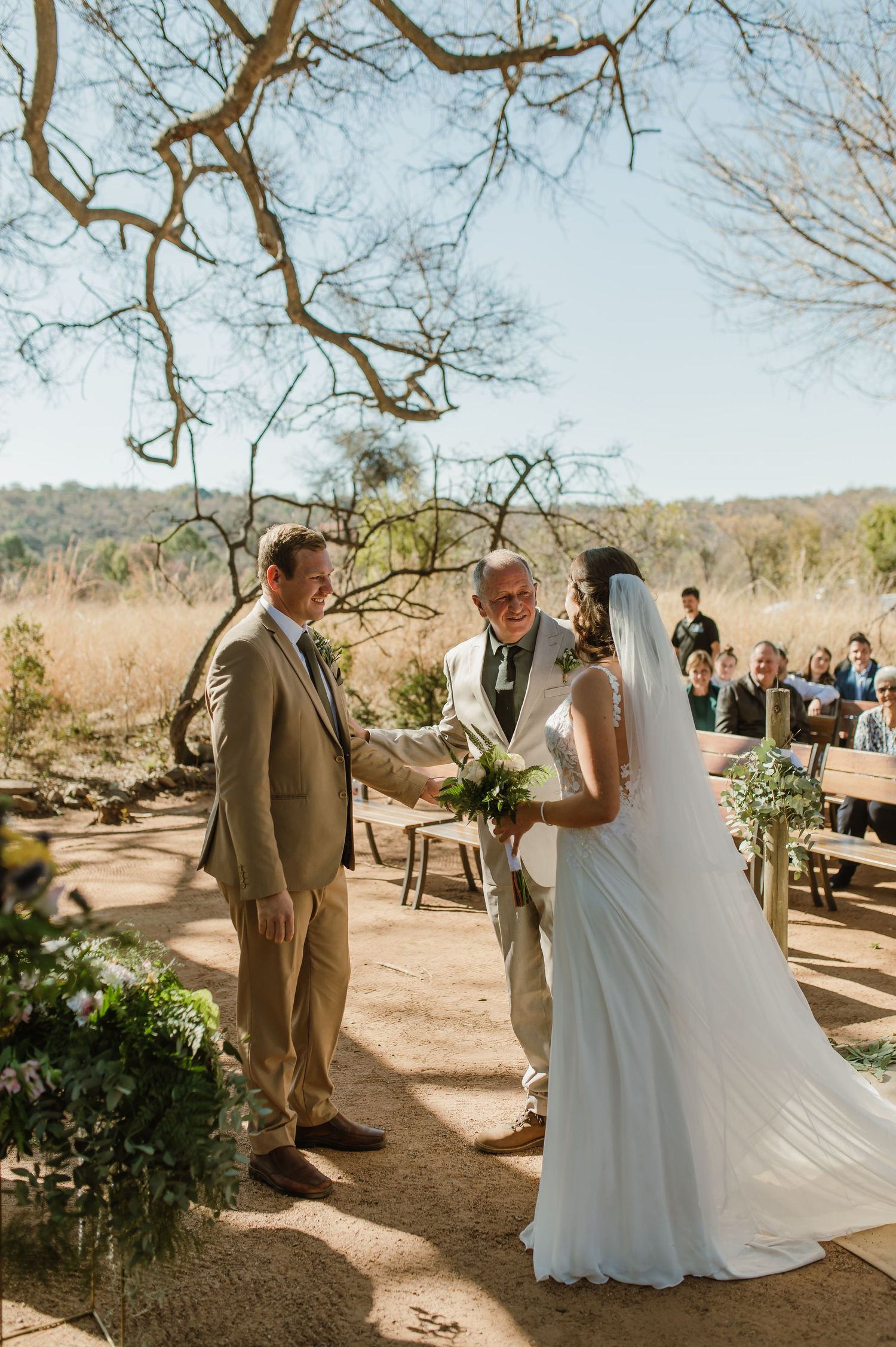 Desert wedding ceremony with couple exchanging vows under twisted tree branches.