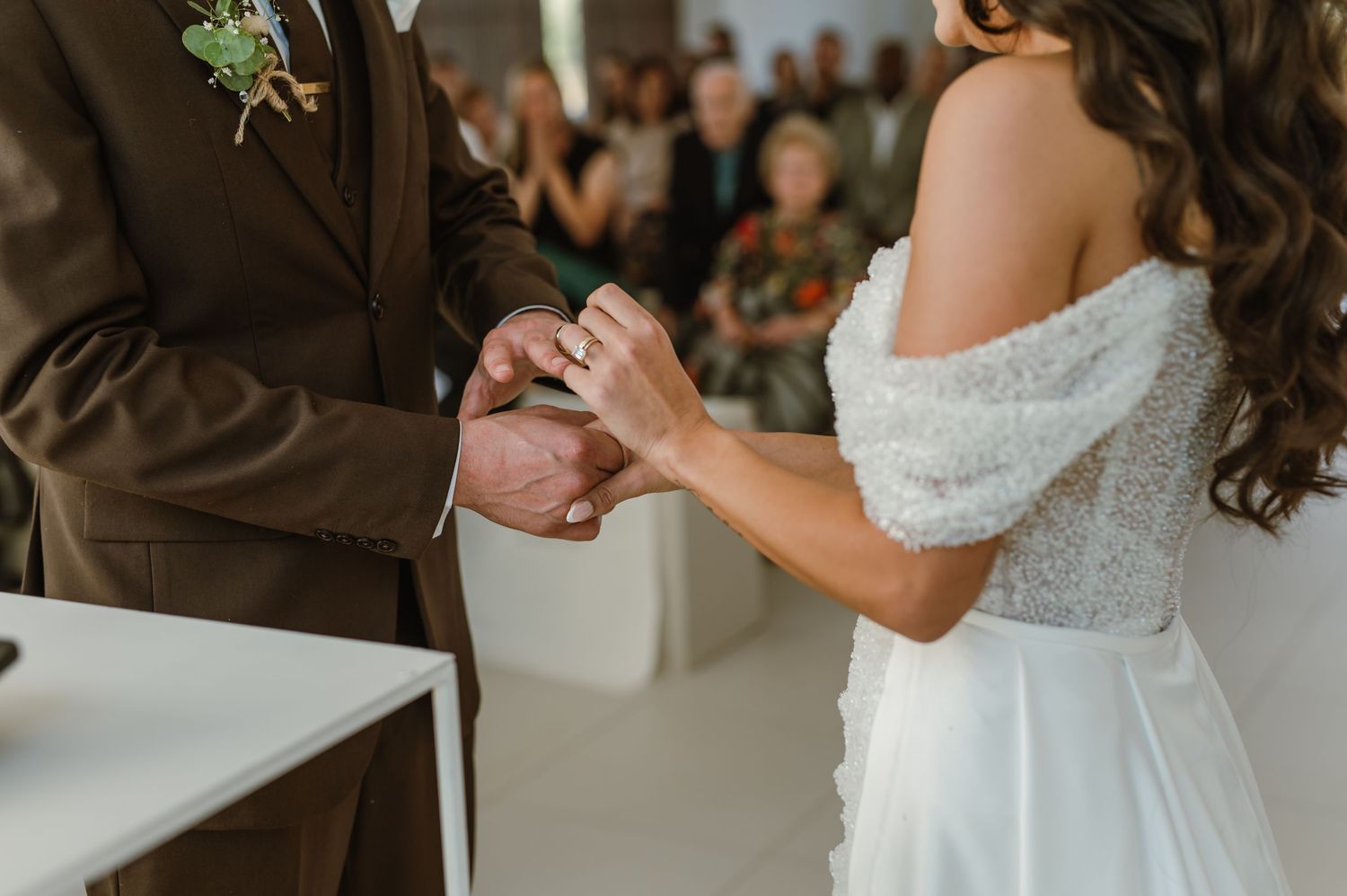 Close-up of hands during wedding ring exchange ceremony in bright indoor setting.