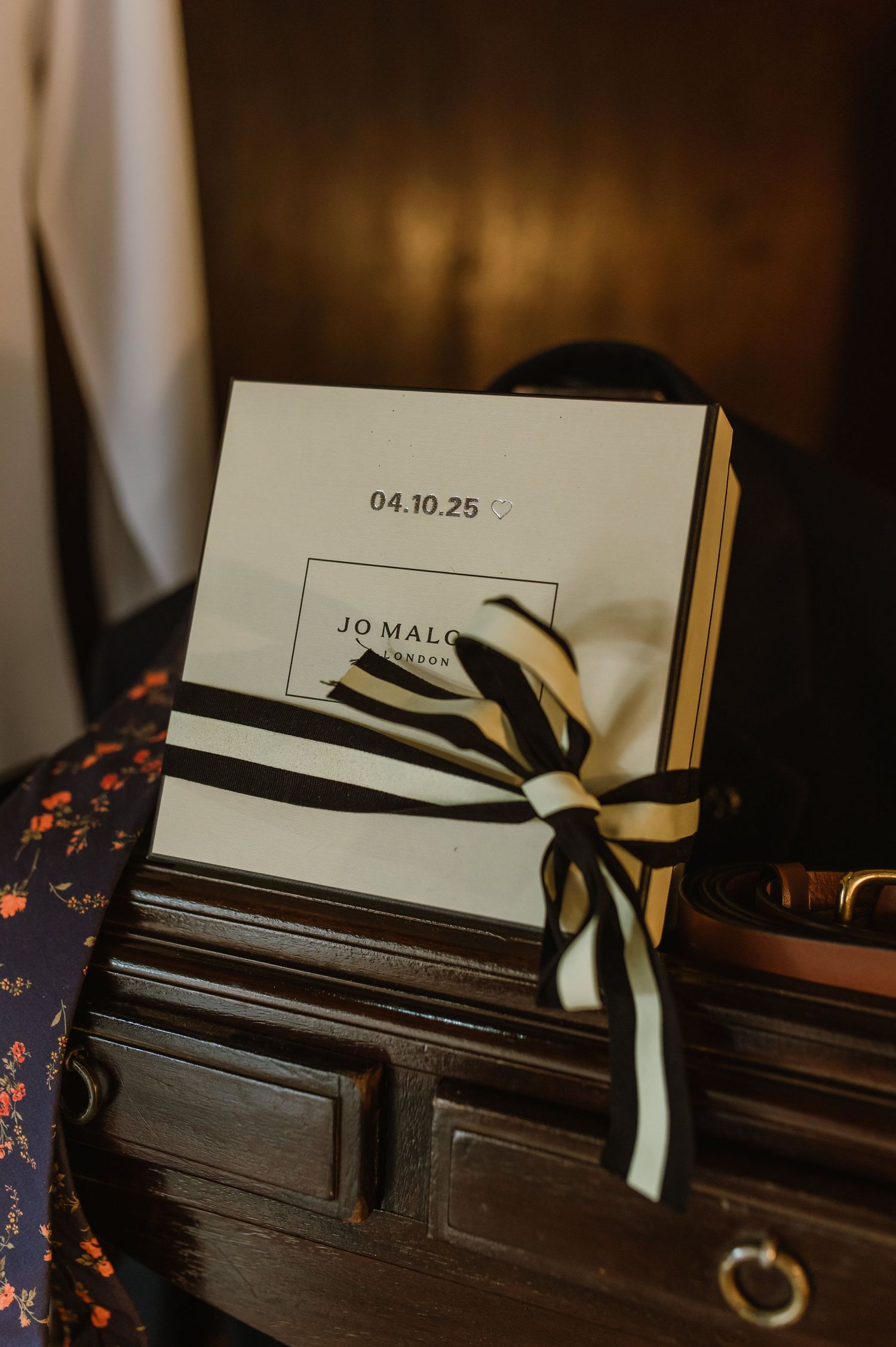 Jo Malone branded boxes with black and white ribbon displayed on dark wooden surface.