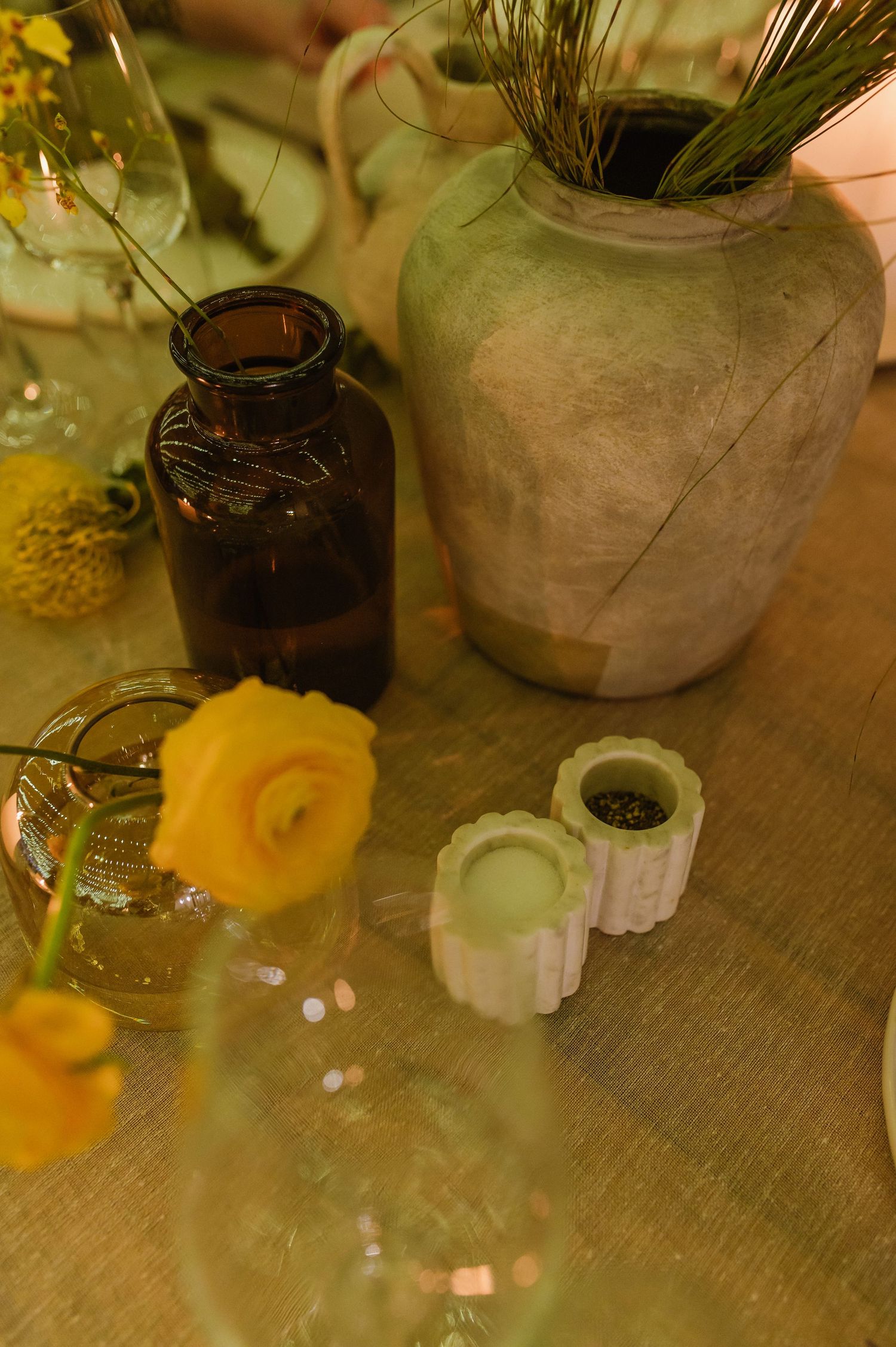 Rustic table decor featuring glass vases with orange flowers and greenery on wooden surface.