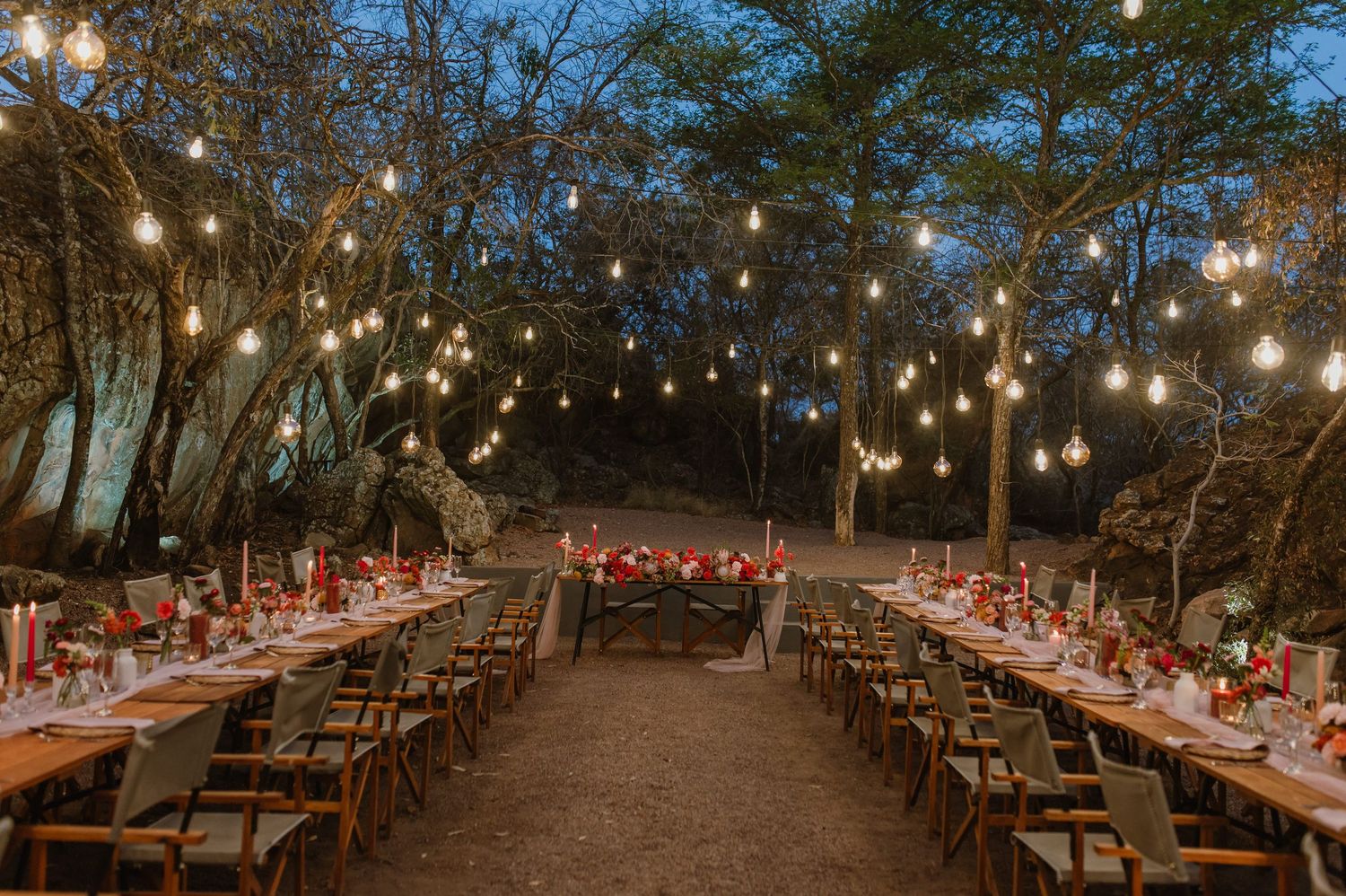 String lights illuminate outdoor wedding reception tables arranged in long rows.