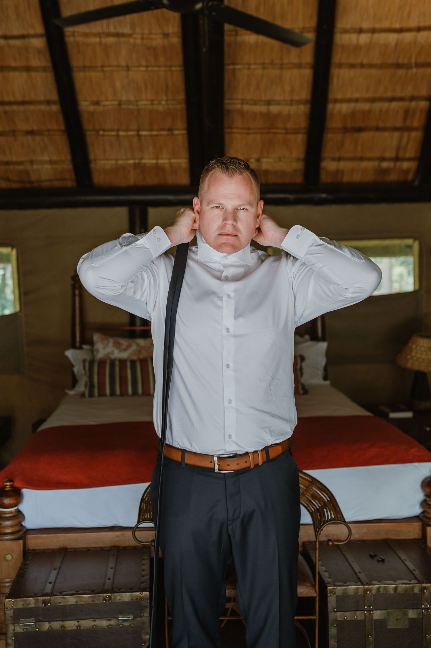 A series of photos showing someone getting dressed in formal attire in a rustic room with thatched roof.