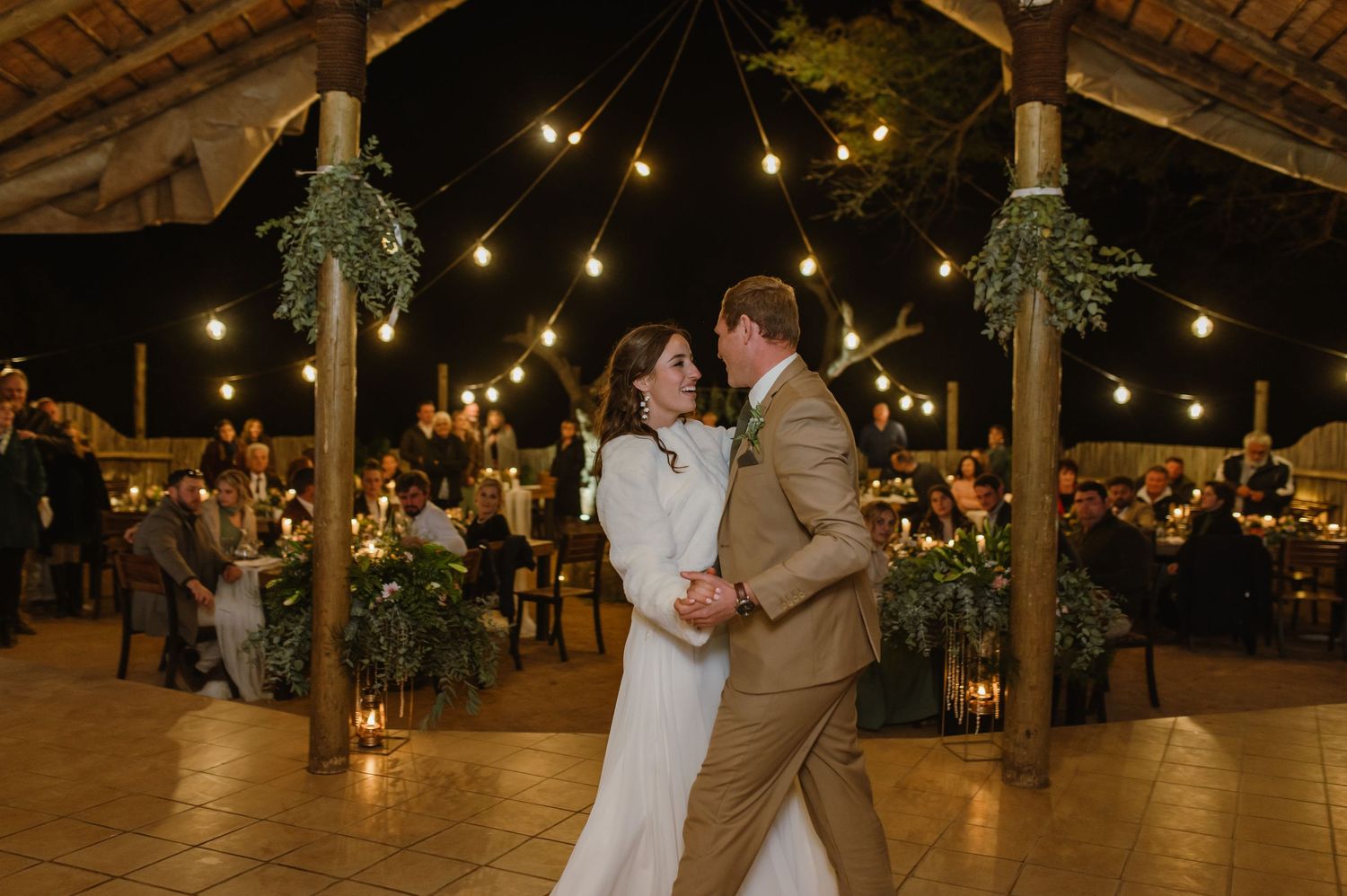 A romantic outdoor wedding reception with string lights and couples dancing on the tiled floor.
