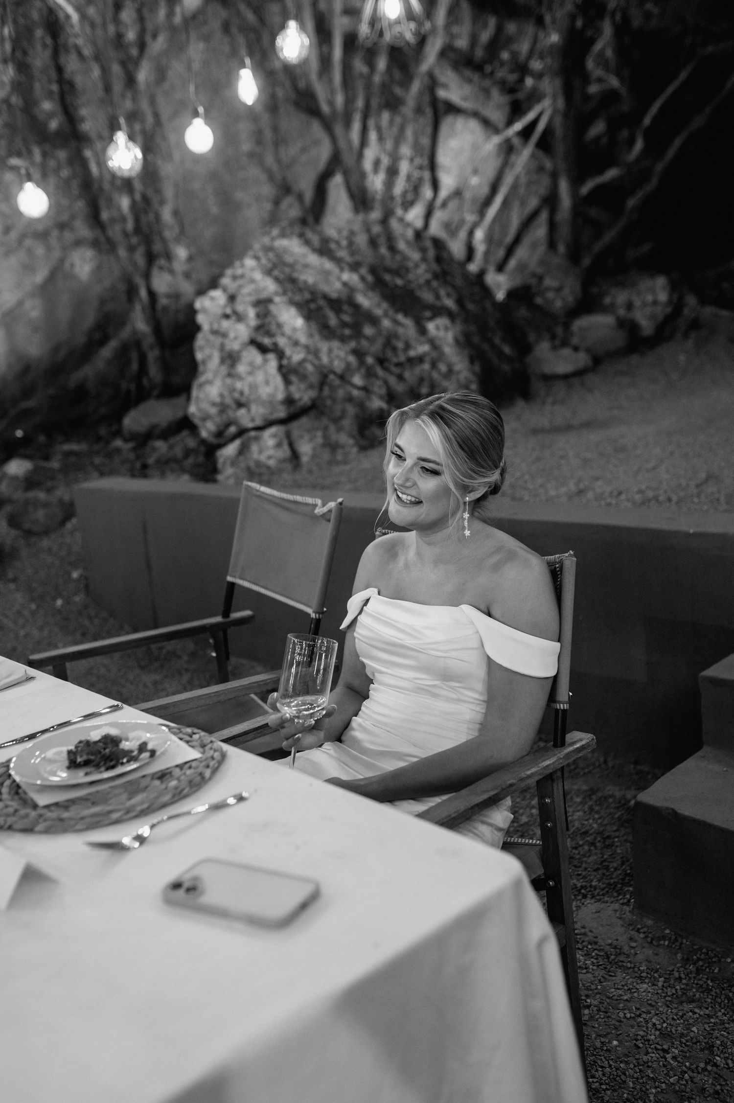 Wedding dinner setup with elegant white tablecloths under twinkling lights in a rustic outdoor setting.