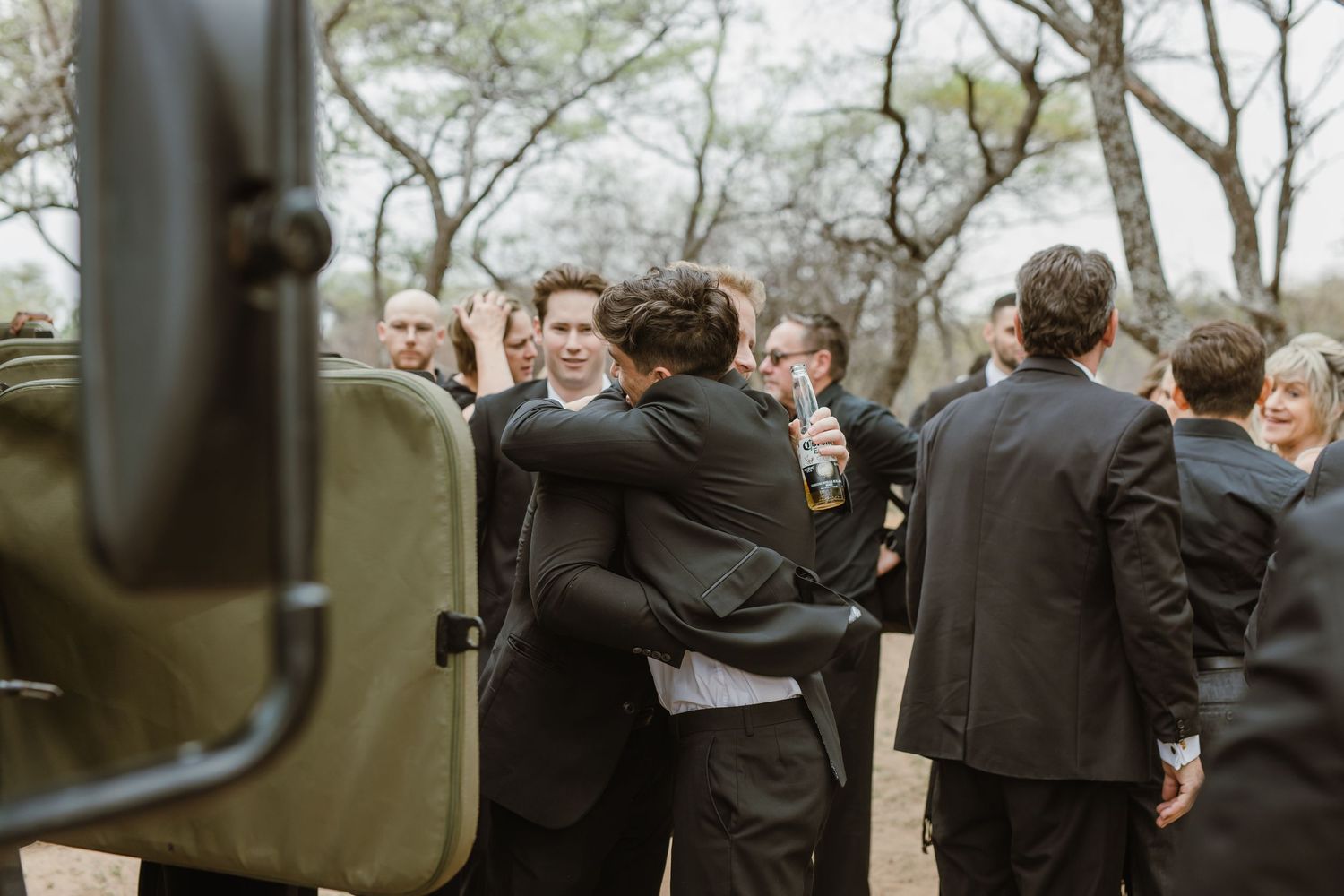 Emotional embraces between wedding guests next to safari vehicles.