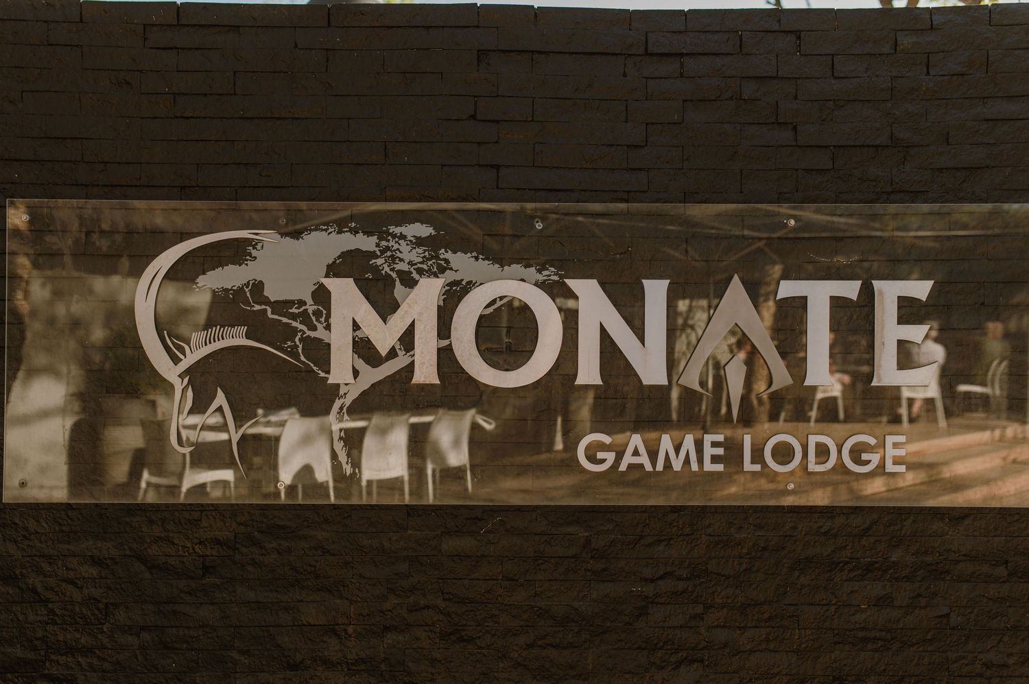 Wooden sign for Monate Game Lodge mounted on dark brick wall.