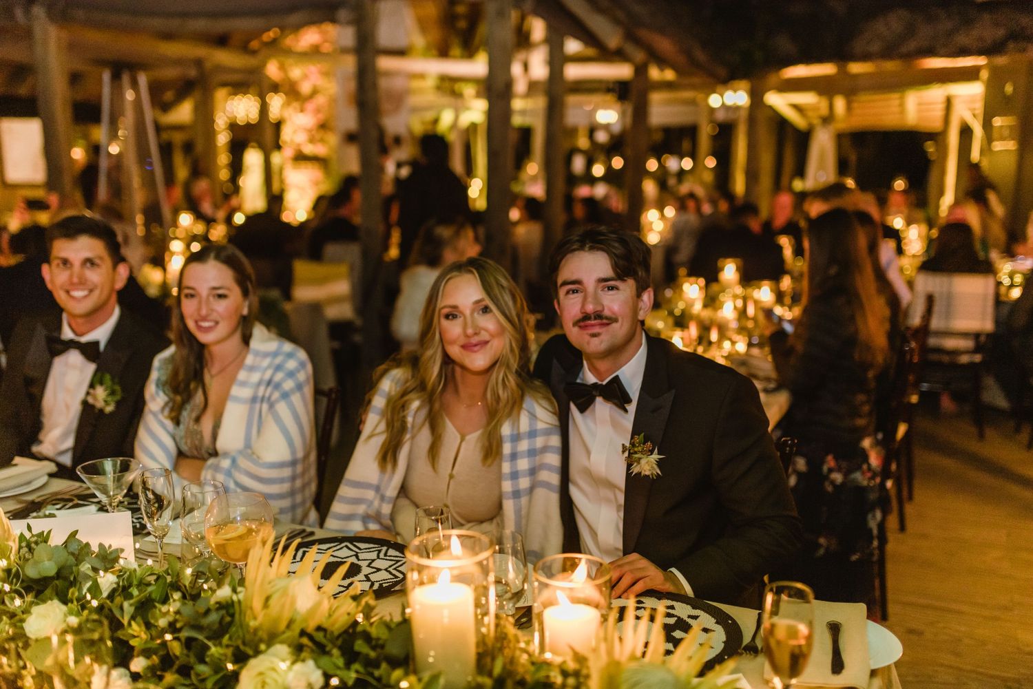 Long banquet tables decorated with greenery and candles at an outdoor evening wedding reception.