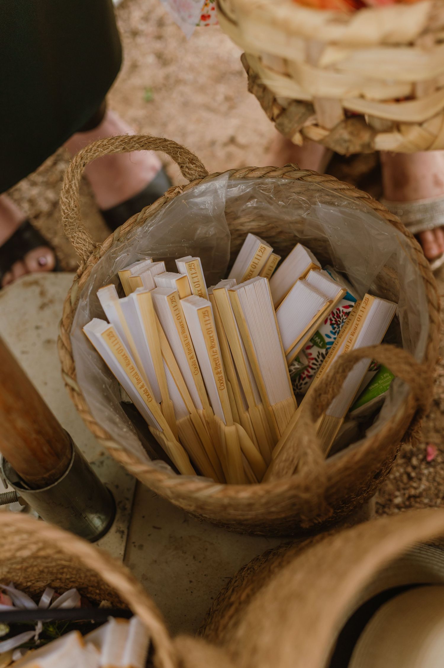 Woven basket filled with paper hand fans for guests at an outdoor wedding ceremony.