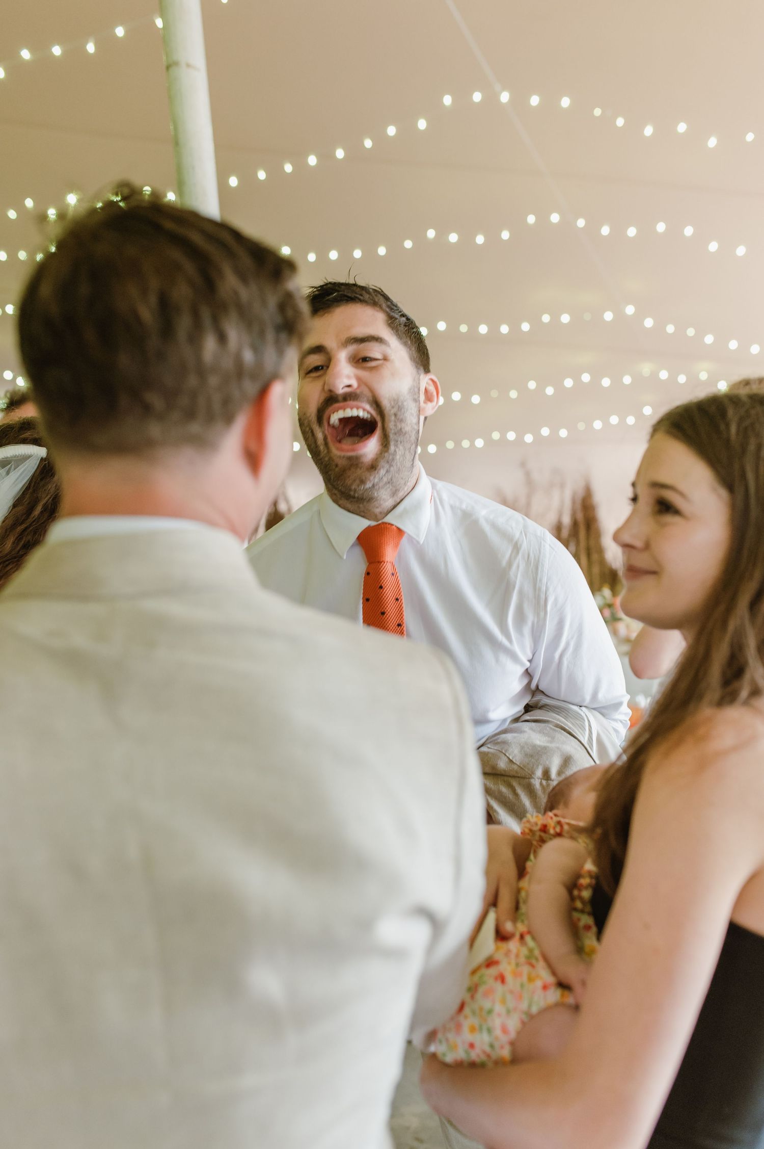 Wedding reception guests dancing and celebrating under string lights indoors.