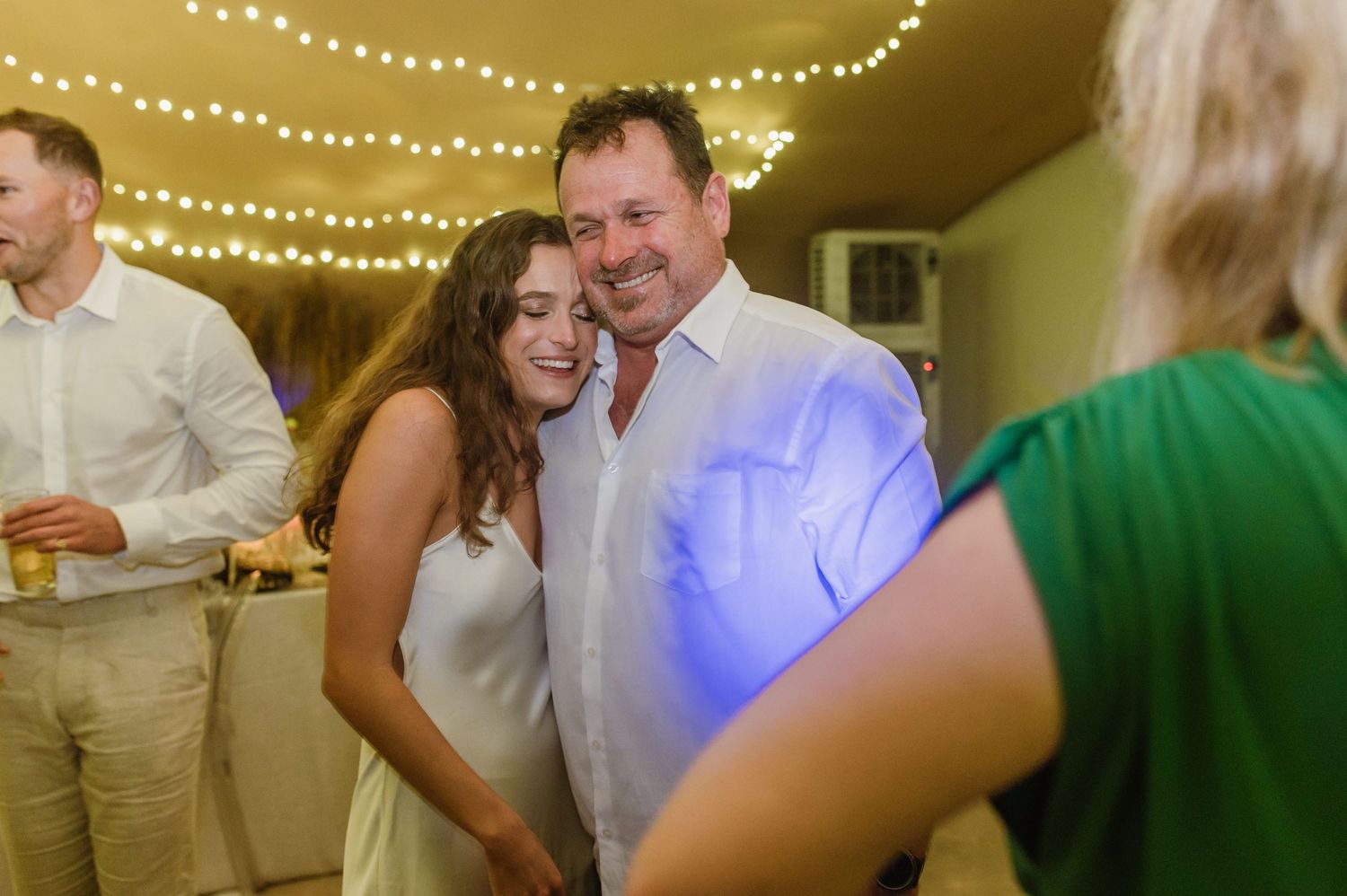 Joyful celebration moments captured under warm string lights at indoor wedding reception.