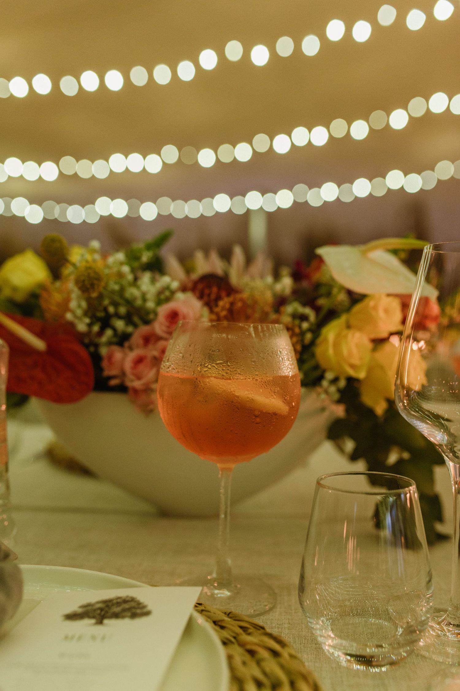 Wedding reception tables with cocktails, string lights, and floral centerpieces.