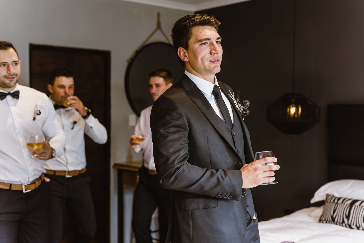 Groomsmen in dark suits sharing drinks during wedding day preparations.