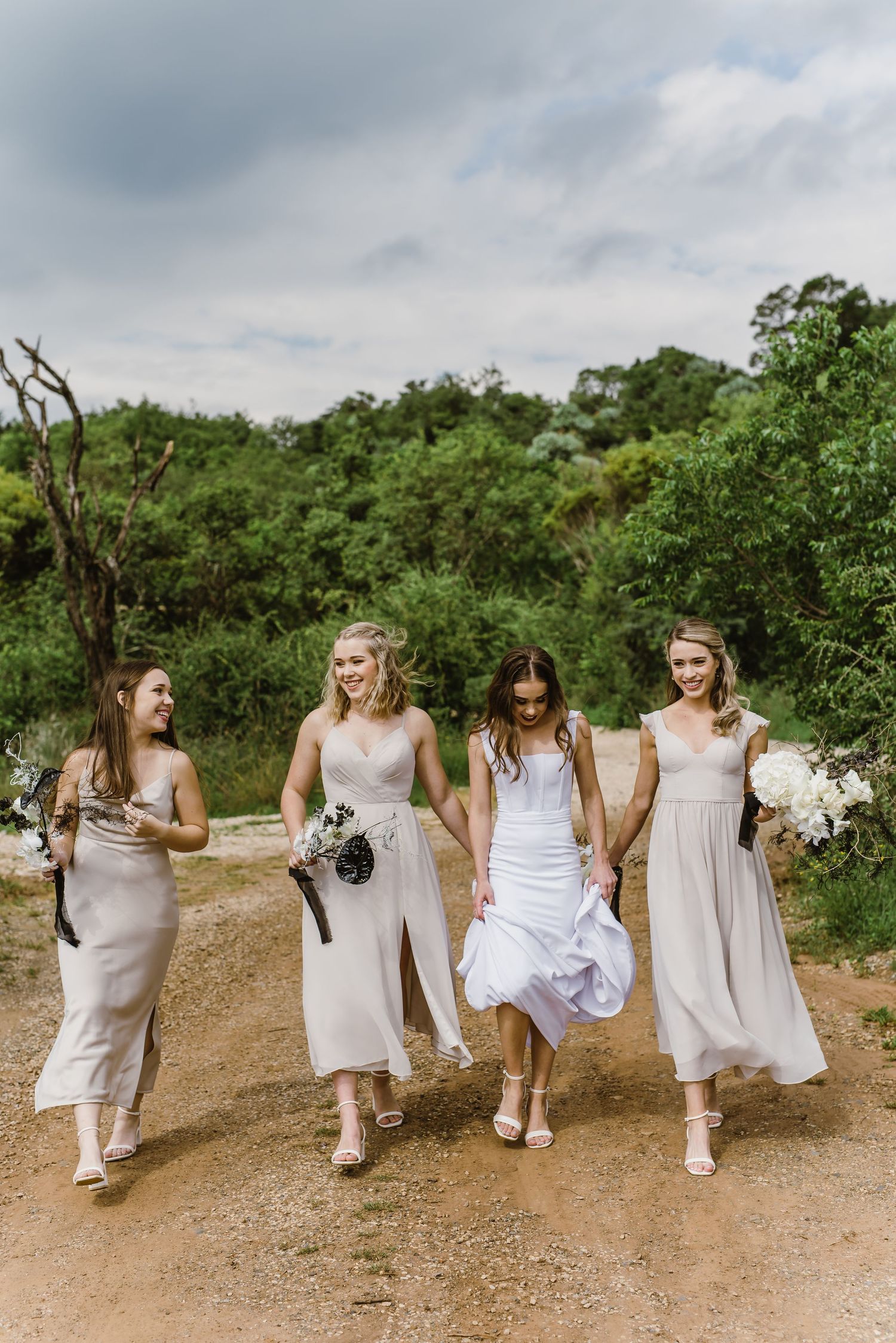 Candid shot of bridal party walking and laughing together on dirt trail.