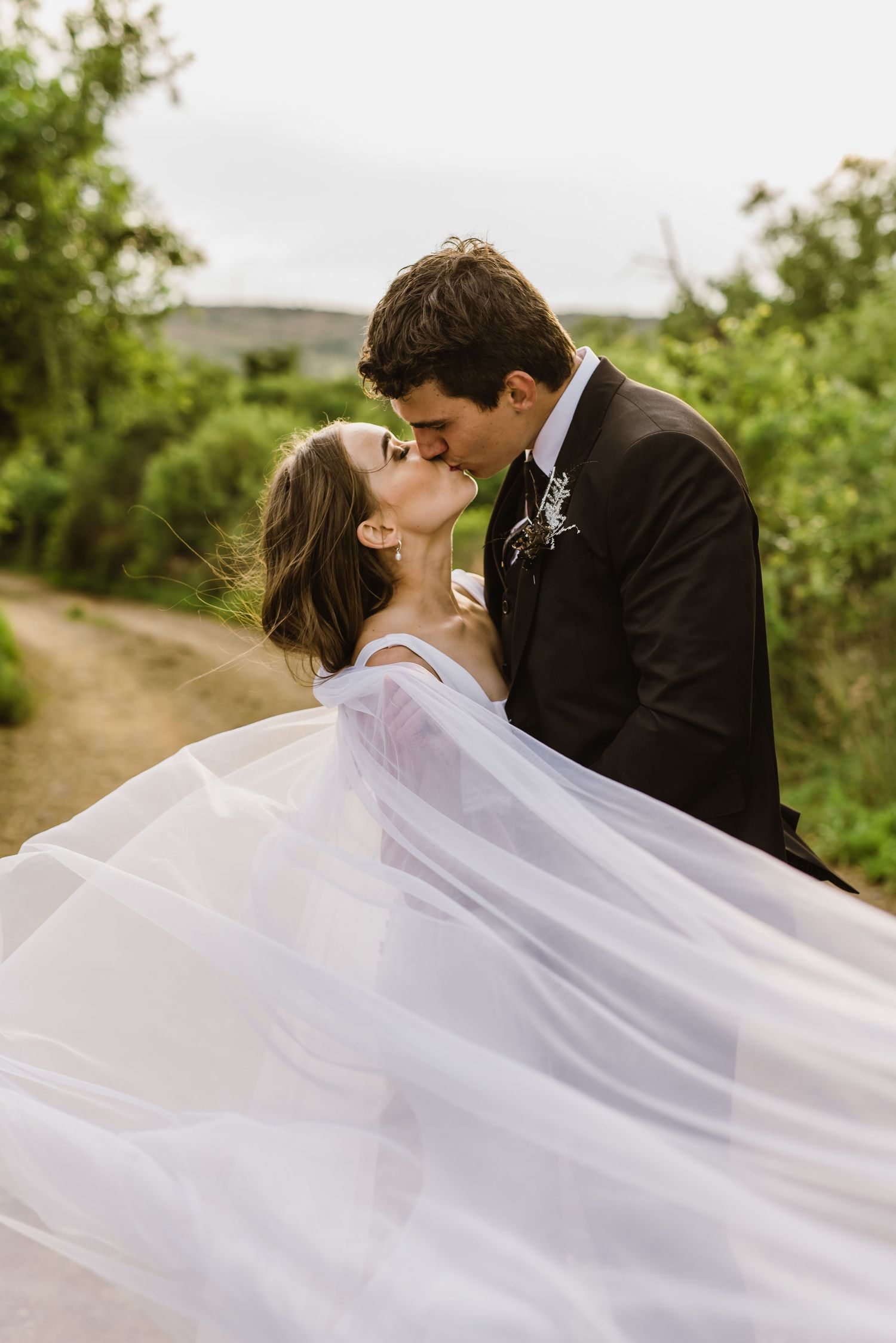 Newlyweds kiss while white veil flows dramatically in desert landscape.
