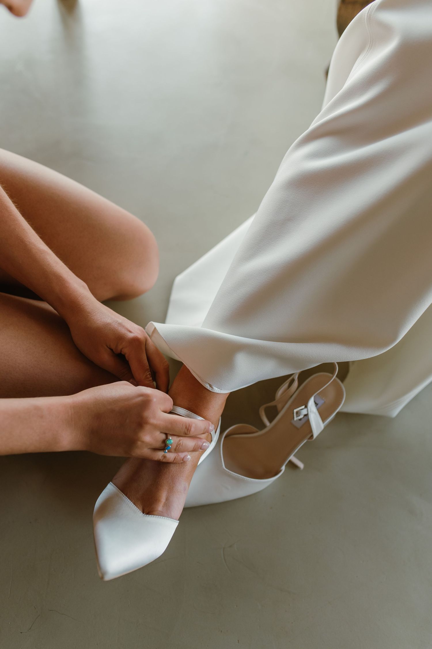 Close-up of hands adjusting the hem of a white wedding dress.