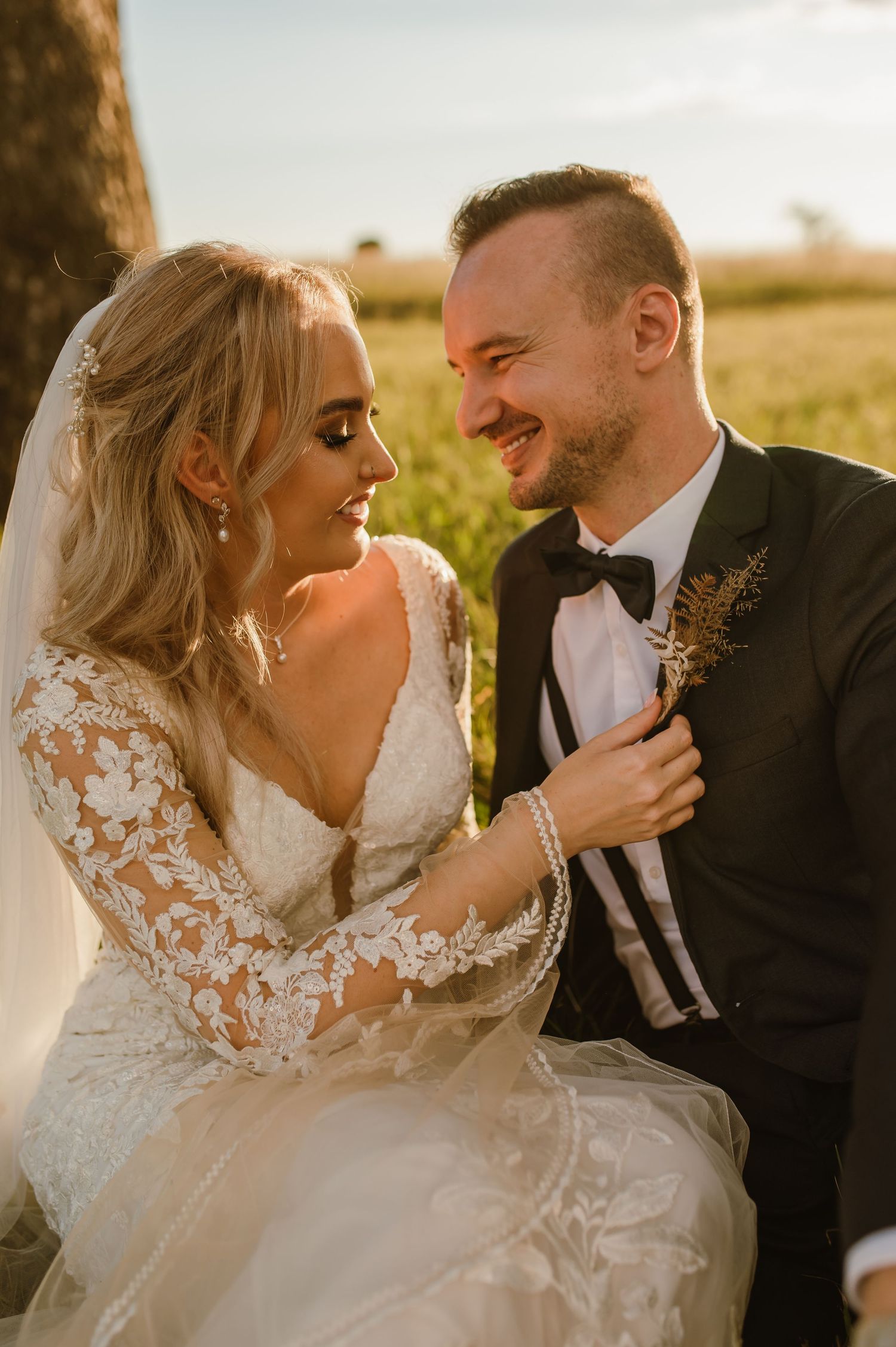 A romantic sunset wedding portrait shows a couple sharing an intimate moment in a lace gown and black tuxedo.