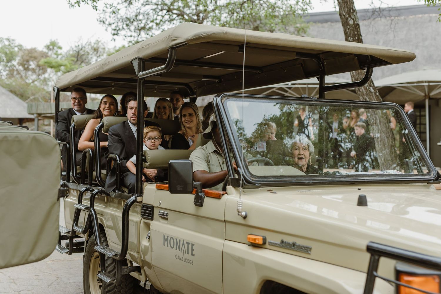 Wedding party riding in an open-air safari vehicle through nature.