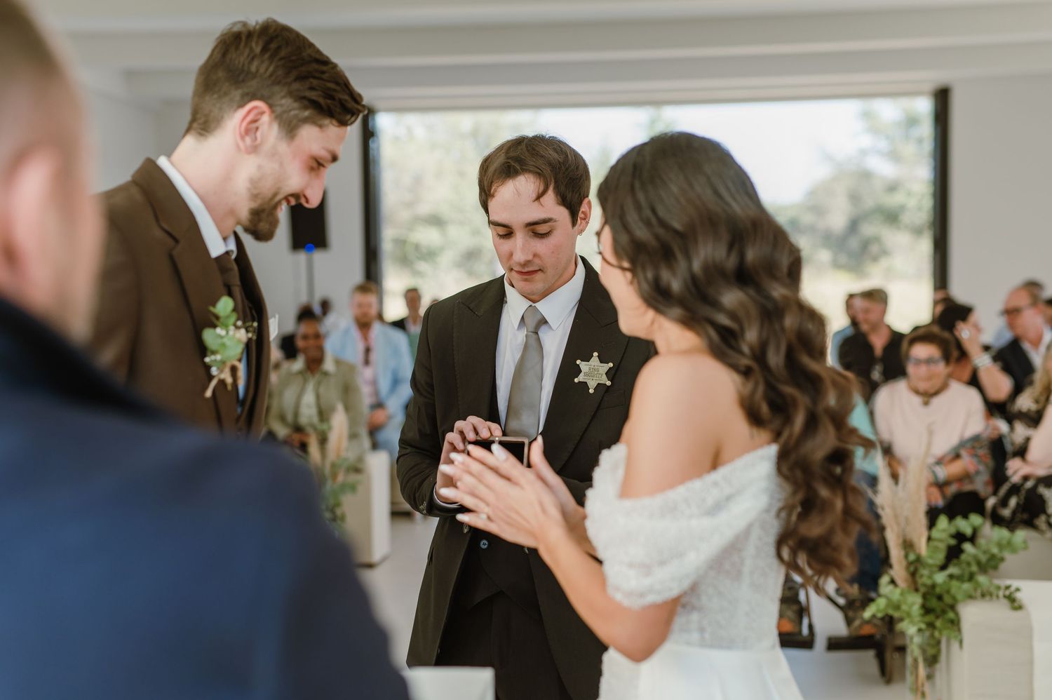Couple exchanges vows during intimate indoor wedding ceremony with guests watching in background.
