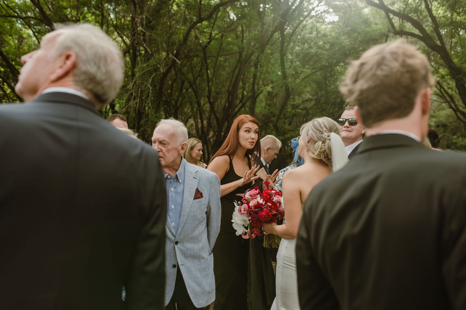 Wedding guests mingling and celebrating on a shaded woodland path during an outdoor ceremony.
