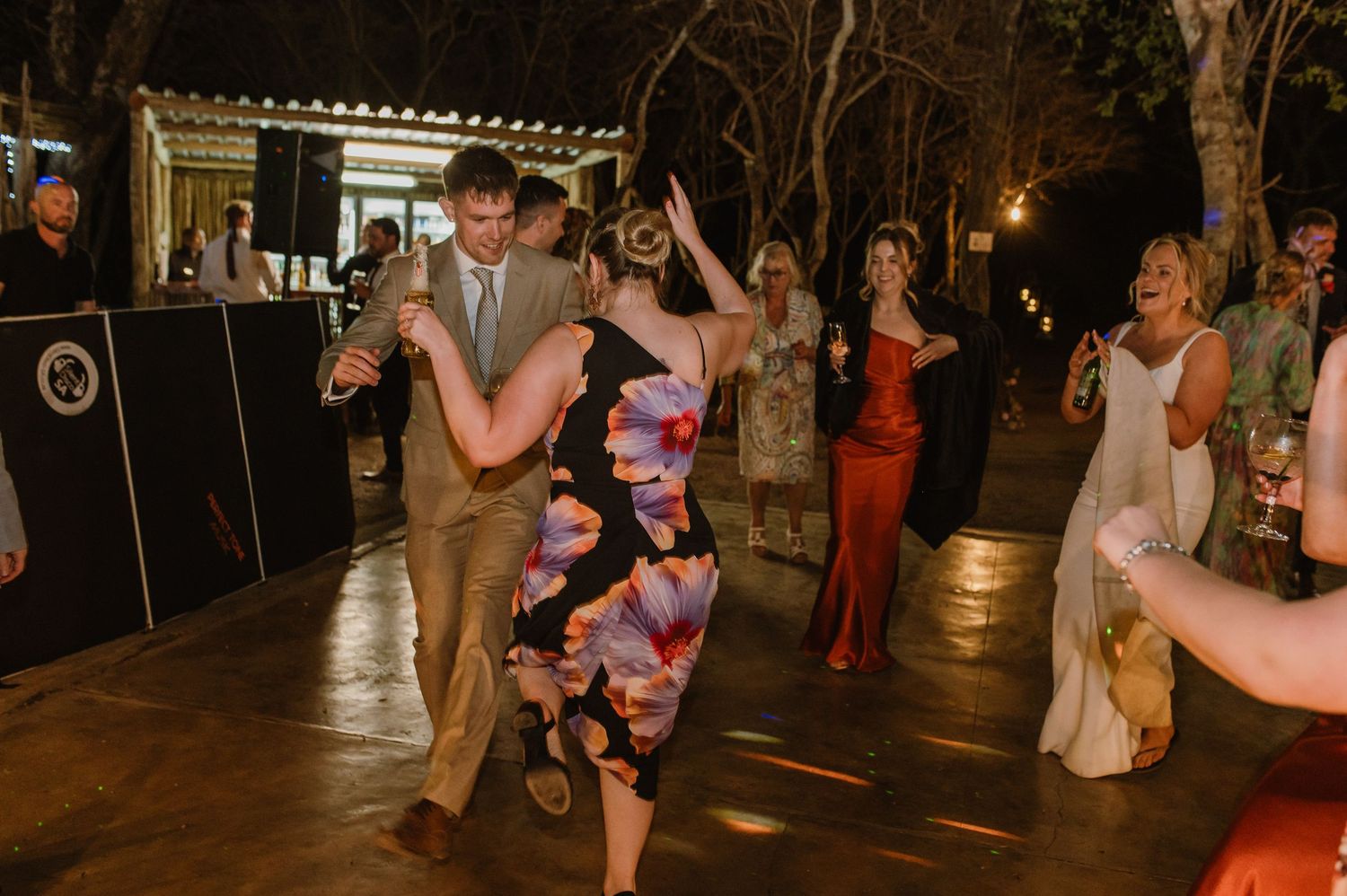 Guests dance and celebrate at a nighttime wedding reception under warm lighting.