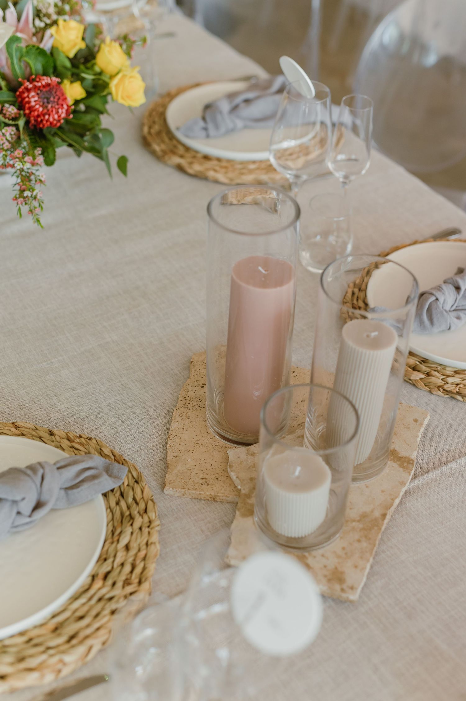 Wedding table decor with blush candles, woven placemats, and delicate floral arrangements.
