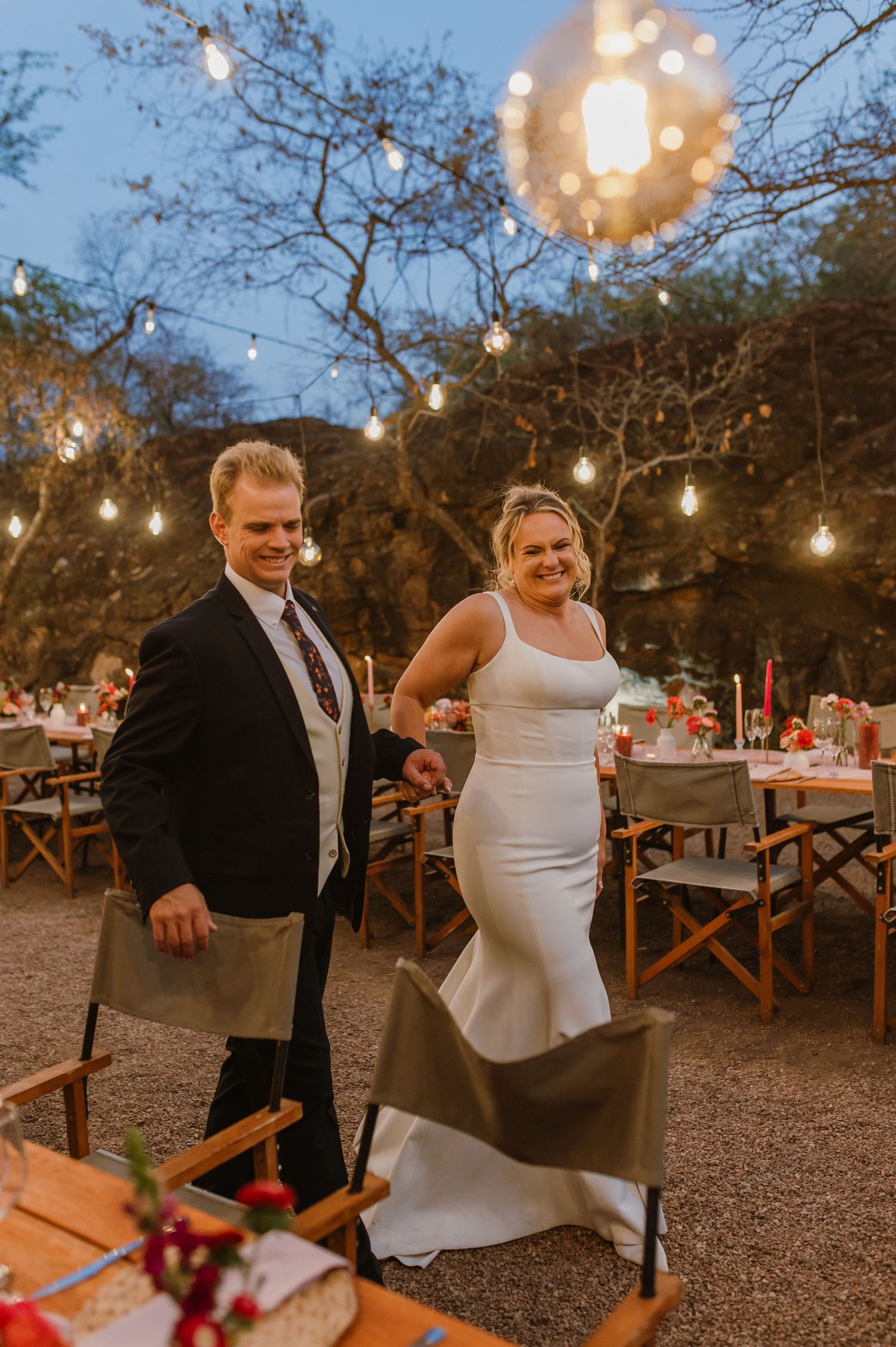A couple dances at an outdoor wedding reception under string lights at dusk.