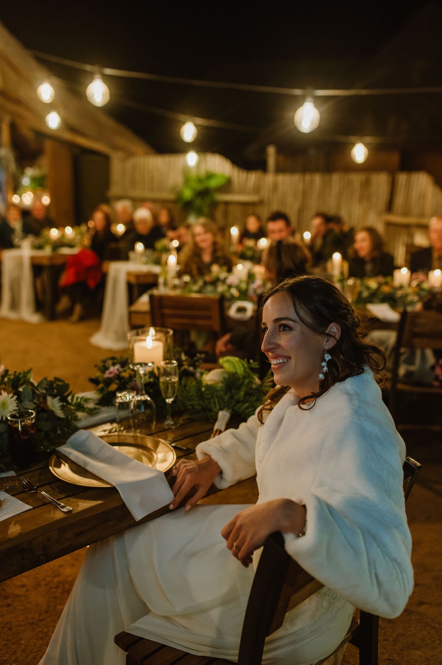 Wedding guests enjoying a candlelit reception dinner under string lights with white table settings.