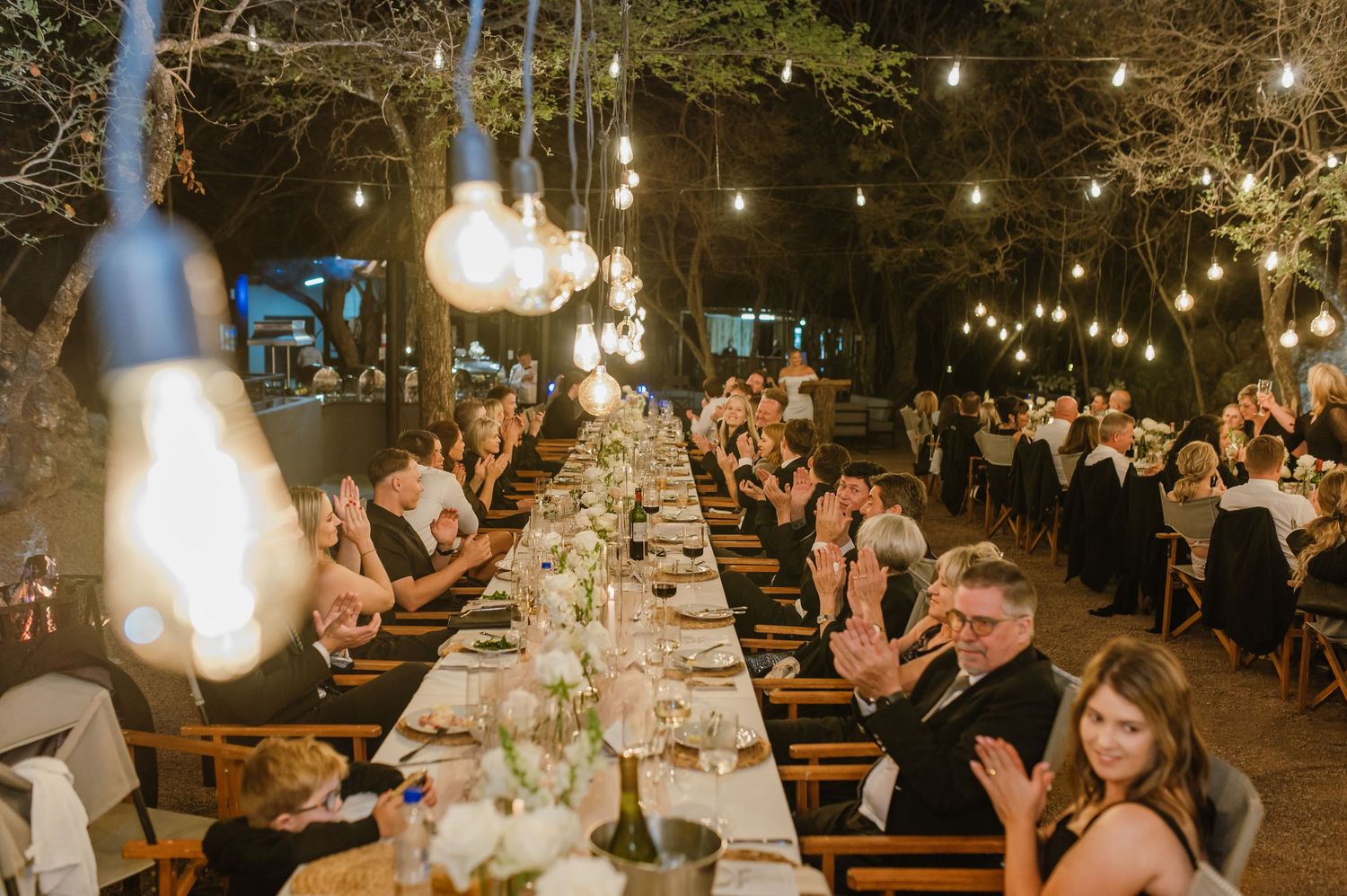 Atmospheric evening wedding reception with multiple tables under glowing string lights.
