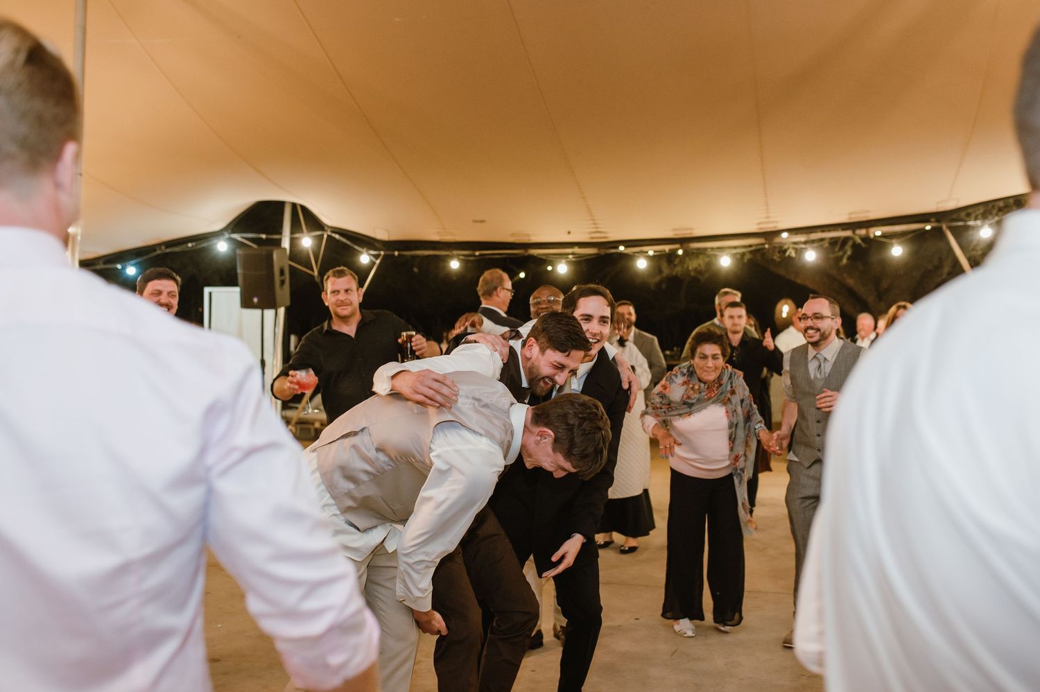 Wedding guests perform energetic dance moves as others watch during the reception celebration.