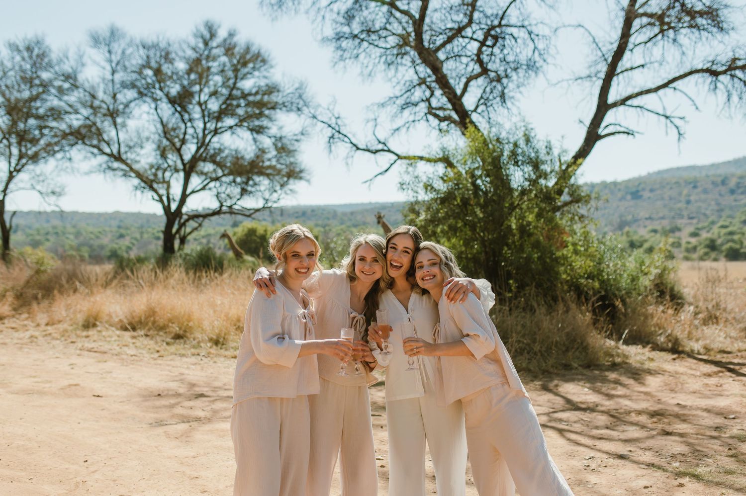 A group poses together in coordinated cream-colored outfits against a desert mountain backdrop.
