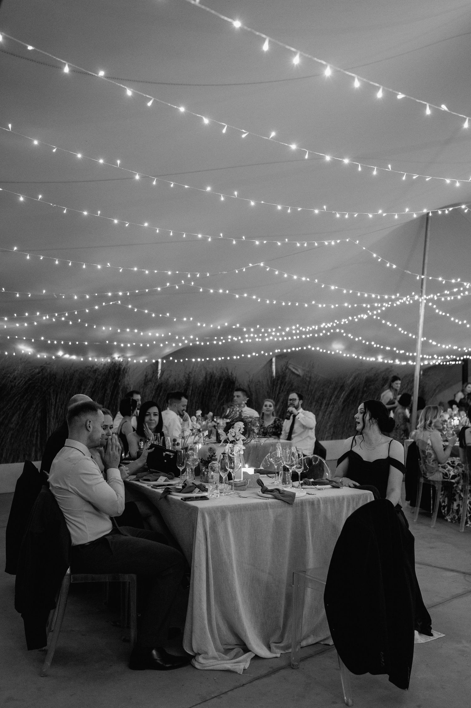 Black and white photo of wedding reception with string lights illuminating guest tables.