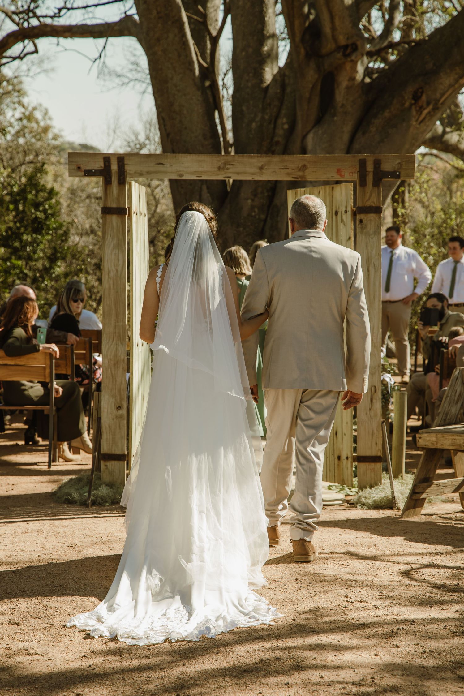 Wedding ceremony procession in a rustic outdoor setting with wooden arch and natural decor.