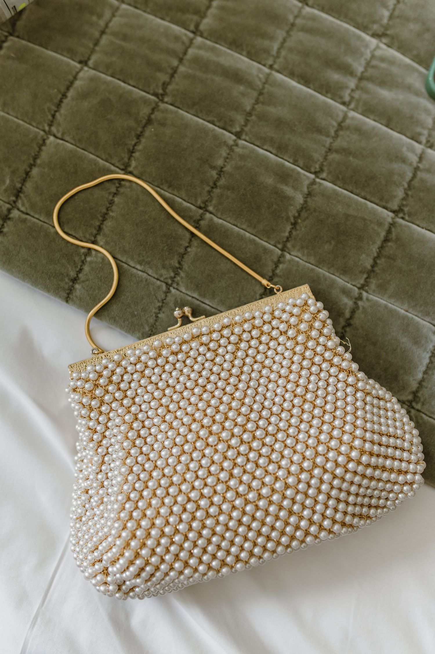 Elegant pearl beaded clutch purse displayed on green quilted fabric.