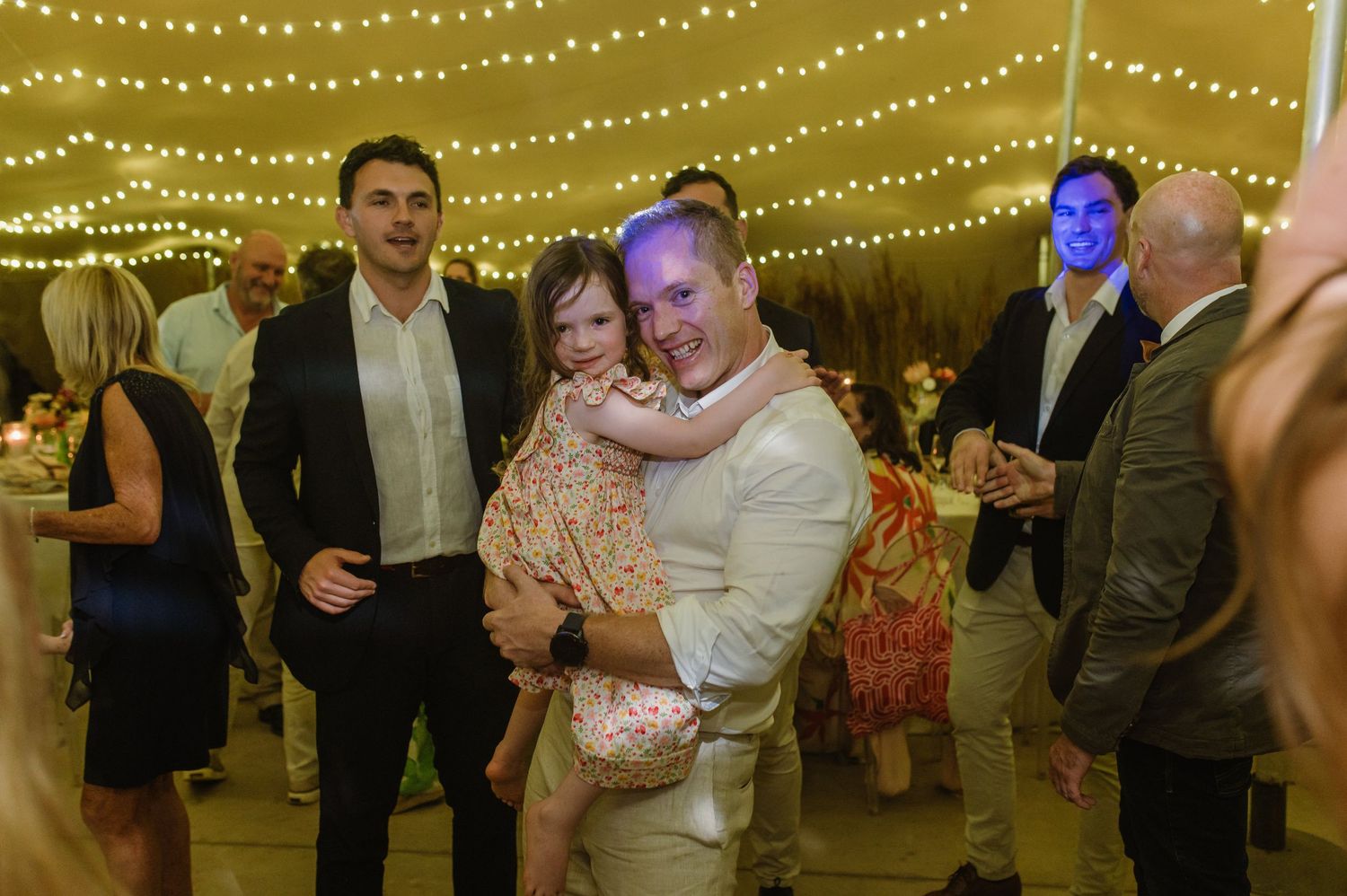 Wedding party members enjoying festivities under warm ambient lighting at indoor reception.