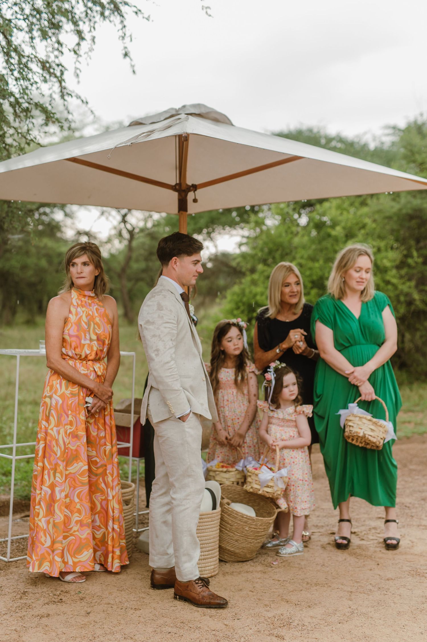 Wedding attendees in colorful summer dresses gather under beige canopies during an outdoor celebration.